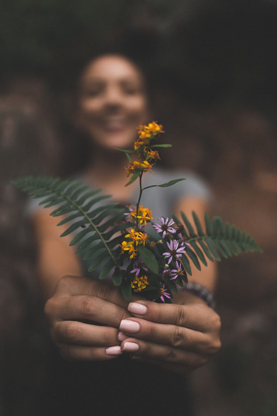 910x1365 HD wallpaper: woman holding orange flower, hand, female, happy, smile, depth of field