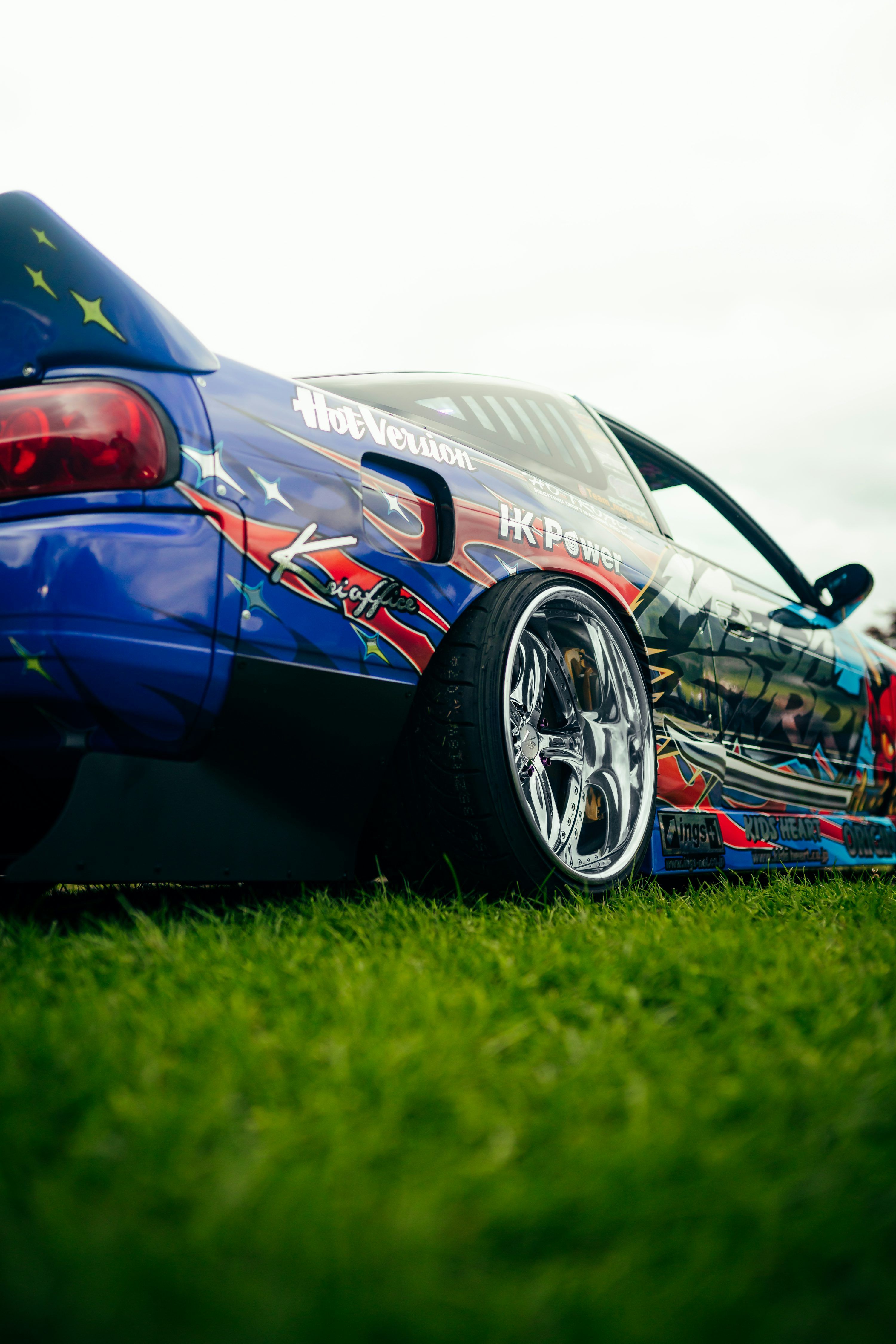 3000x4498 A blue sports car parked on top of a lush green field photo