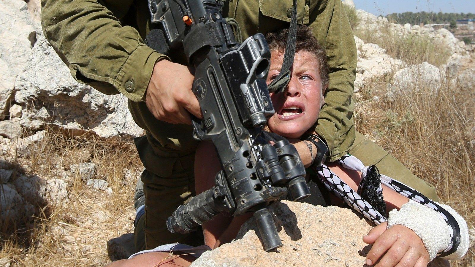 1600x900 image show Israeli soldier handling Palestinian boy