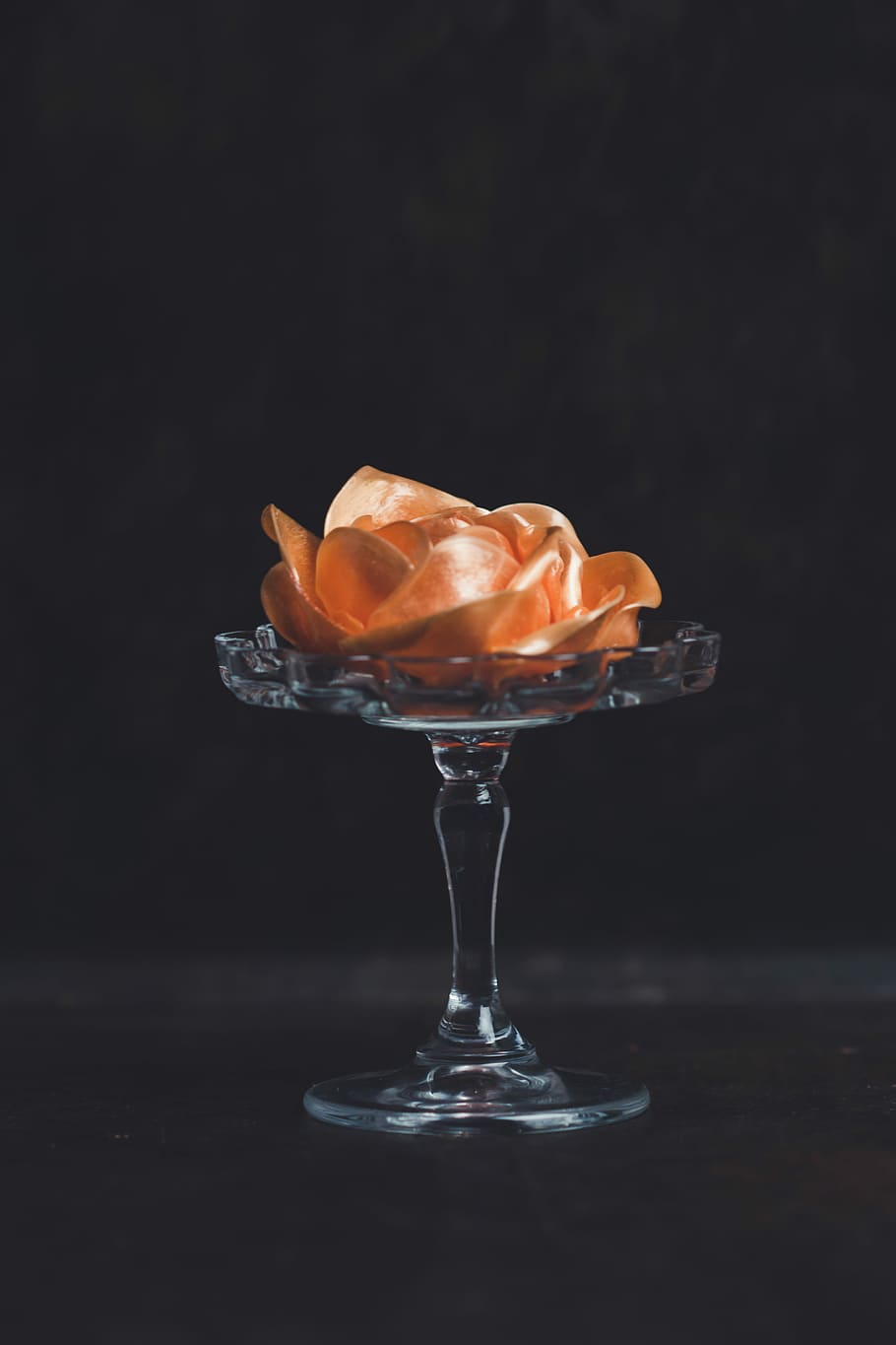 910x1365 HD wallpaper: orange flower on glass footed vase against black background, pink rose on clear glass footed stand