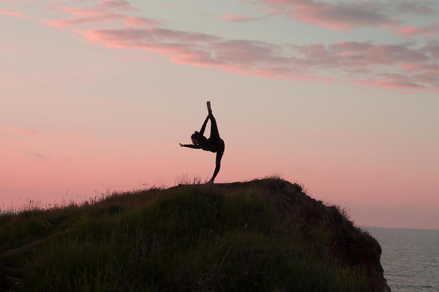 1470x980 Fit woman doing yoga stretching exercise outdoor in beautiful mountains landscape. Female on the rock with sea and sunrise or sunset background training asans. Silhouette of woman in yoga poses 7666020 Stock