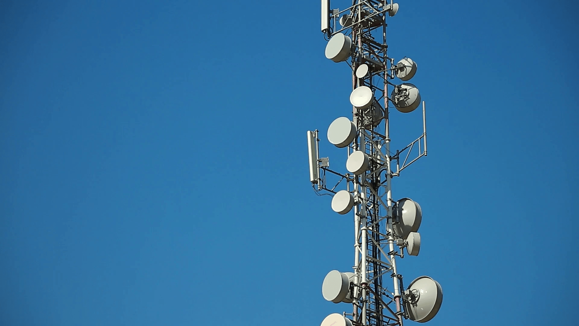 1920x1080 Communication tower antenna on blue background. Cell phone telecommunication tower. Antennas of mobile phone communication, television, internet, radio, on blue sky background