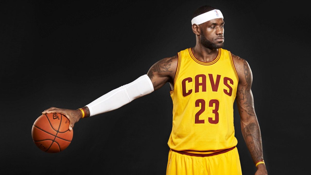 1280x720 LeBron James Is Having Basketball In One Hand Facing One Side In A Black Background Wearing Yellow Sports Dress HD Sports Wallpaper