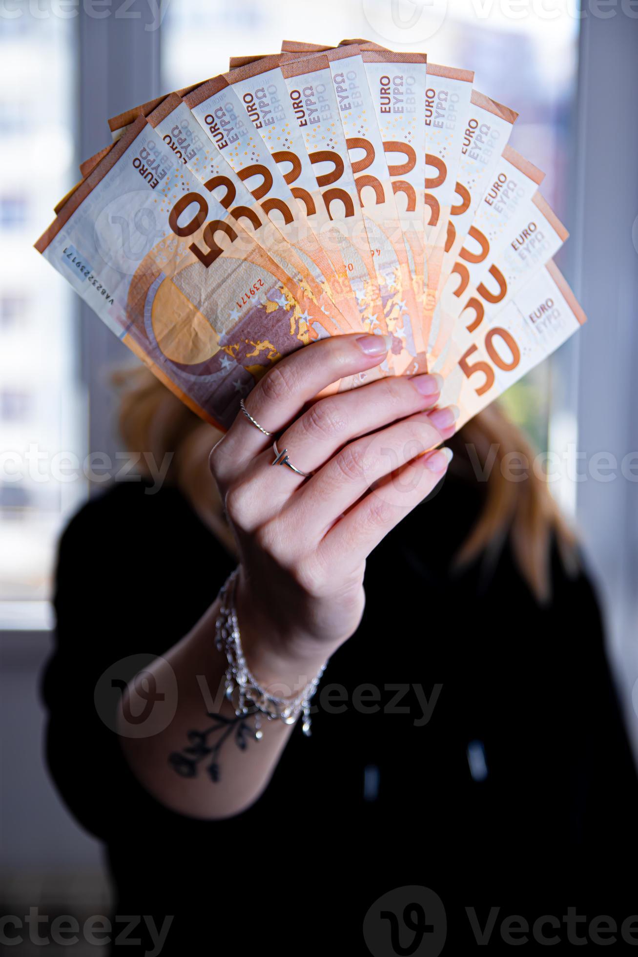 1307x1960 Woman's hand holding a fan of euro banknotes on a black background