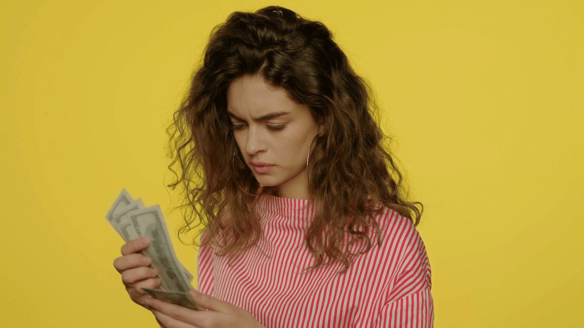 1920x1080 Upset woman counting cash money on yellow background. Unhappy woman count dollar banknotes in studio. Sad girl not enough money cash for shopping
