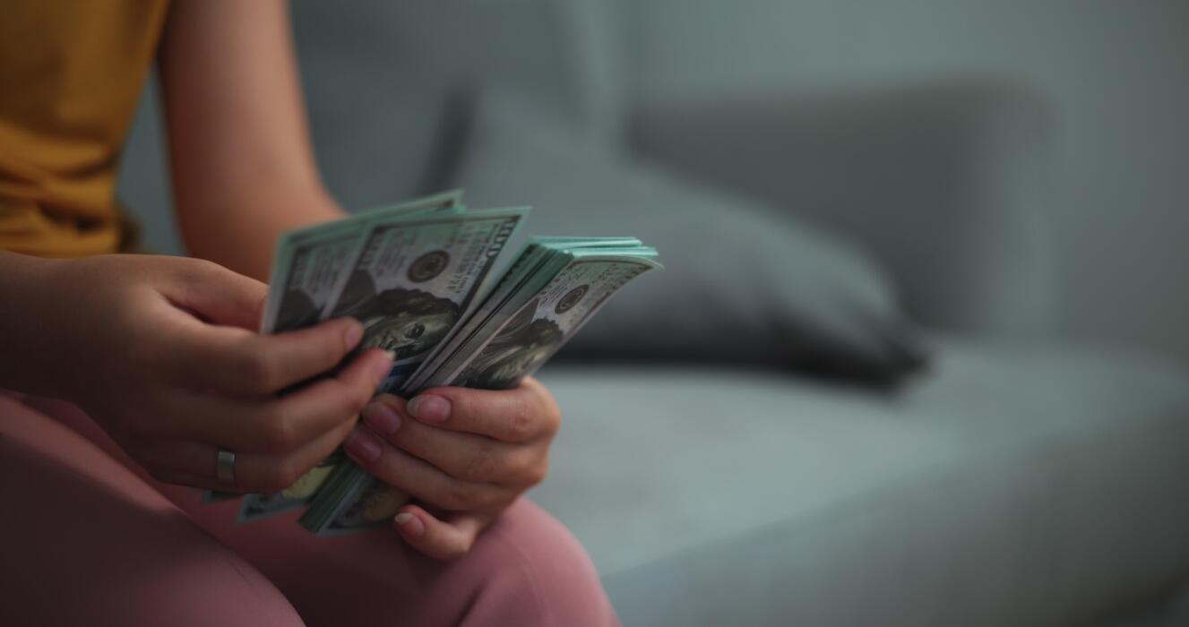 1327x700 Footage close up hands of young Asian woman enjoy counting cash dollars banknotes on sofa in the living room at home
