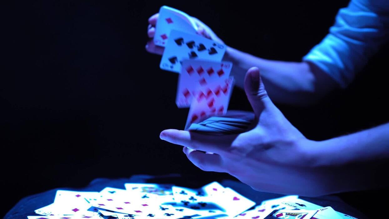 1244x700 Close Up, Hands Of A Magician Performing Tricks With A Deck Of Cards. Blue Lighting. Conjurer Shows Focus. Camera Quickly Rotates 360 Degrees