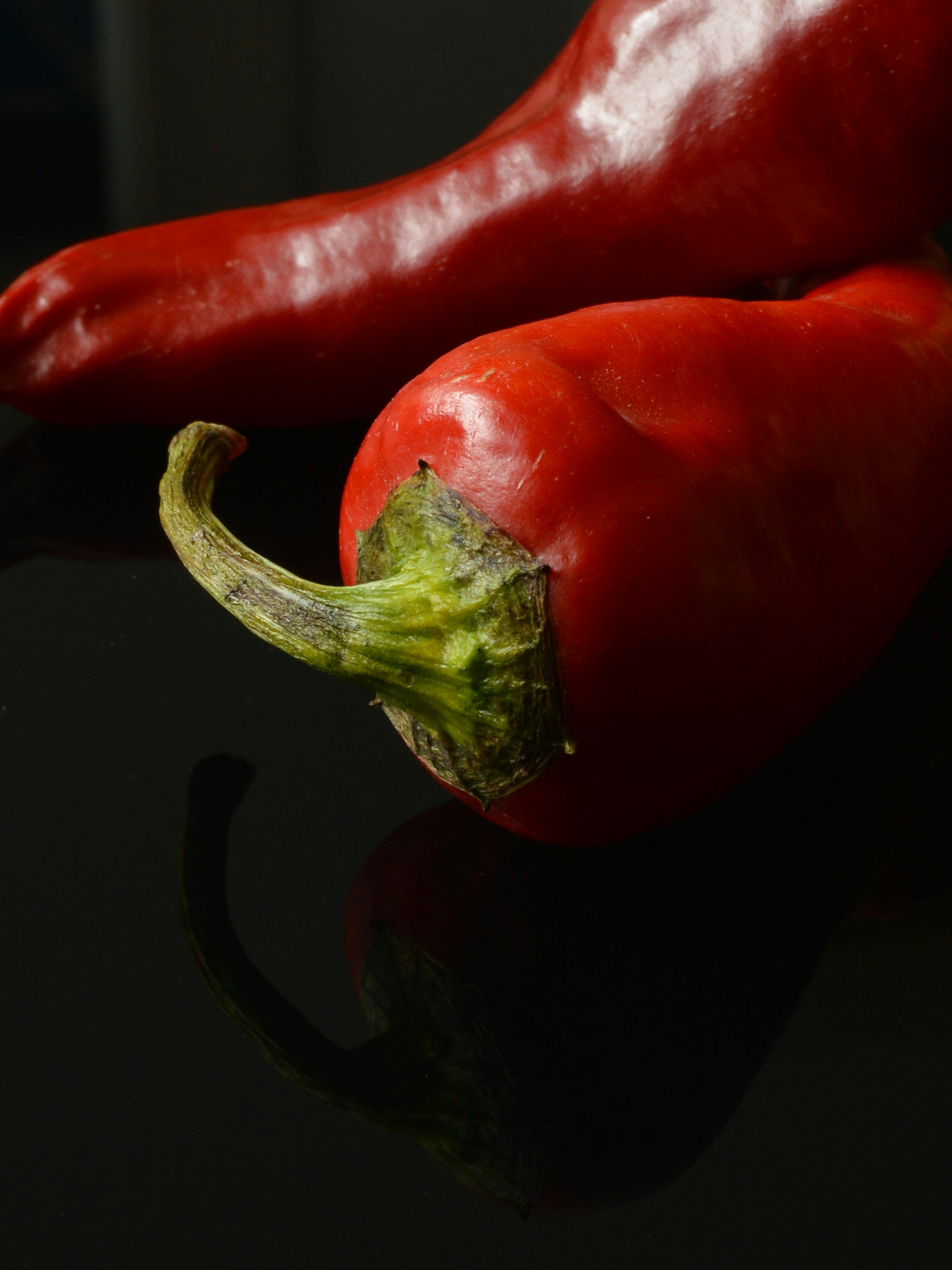 3000x4000 Two red chili peppers on a dark surface. photo