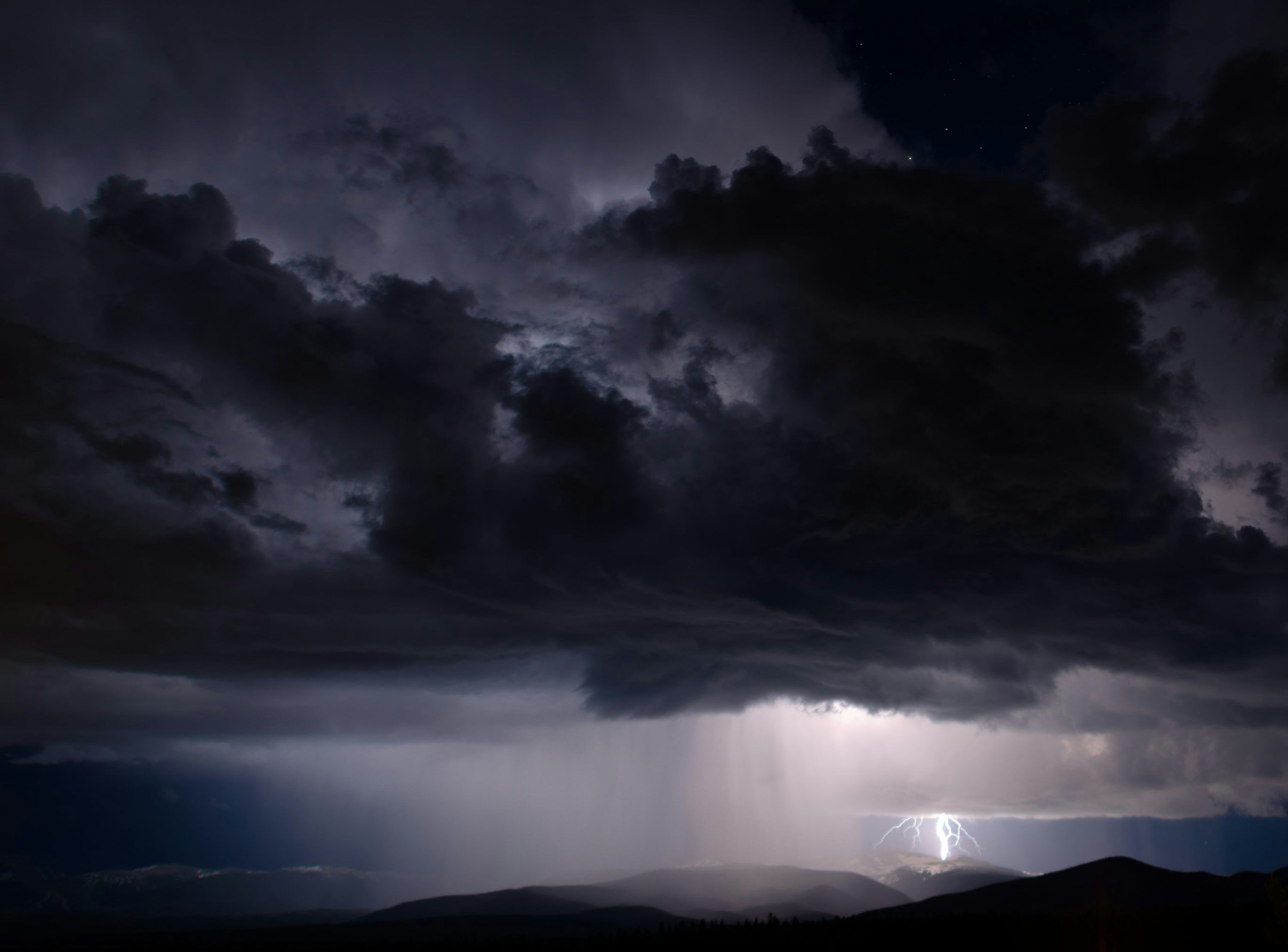 3000x2217 Dark storm clouds loom over a mountain range. photo