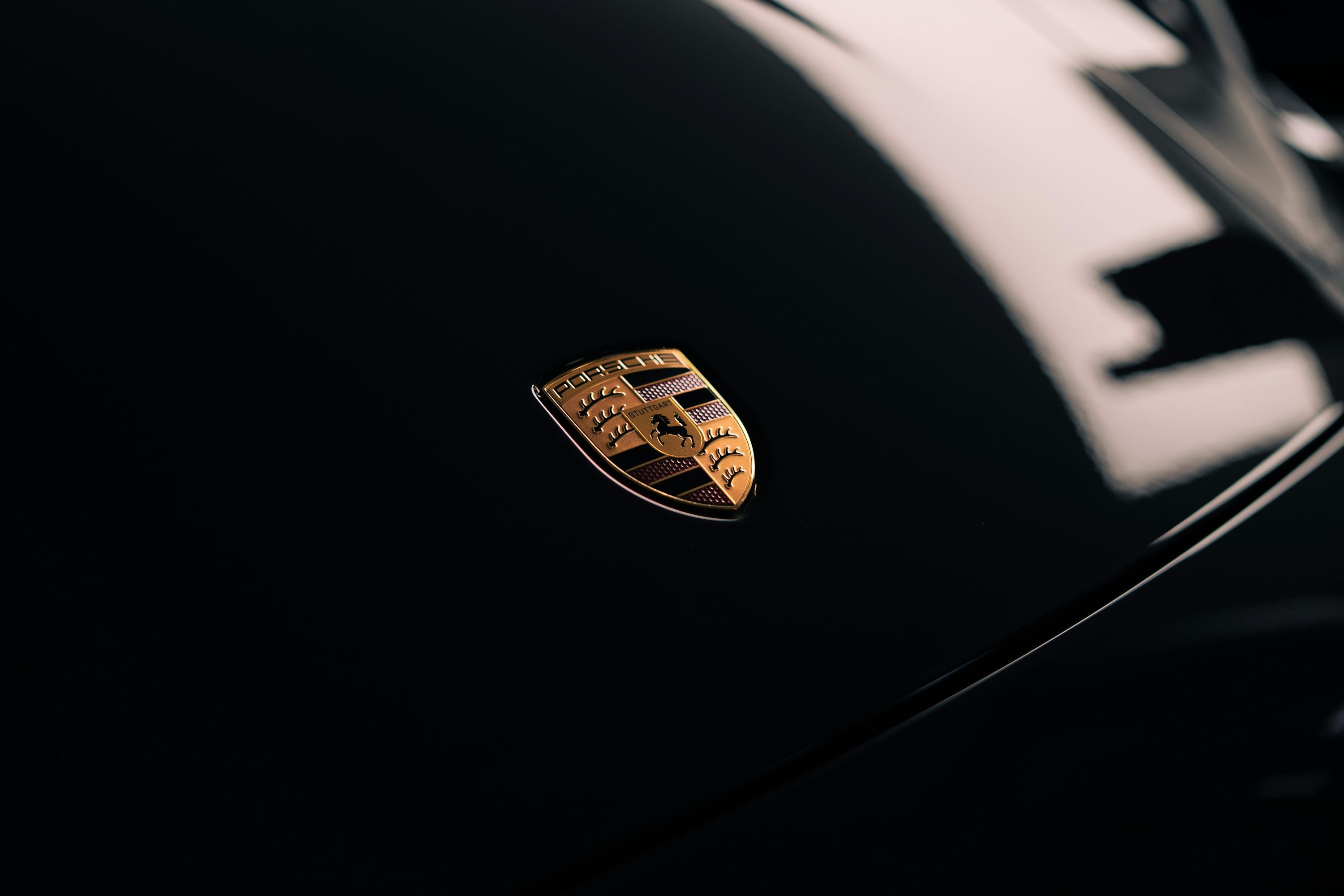 3000x2000 A porsche emblem shines on a black car. photo