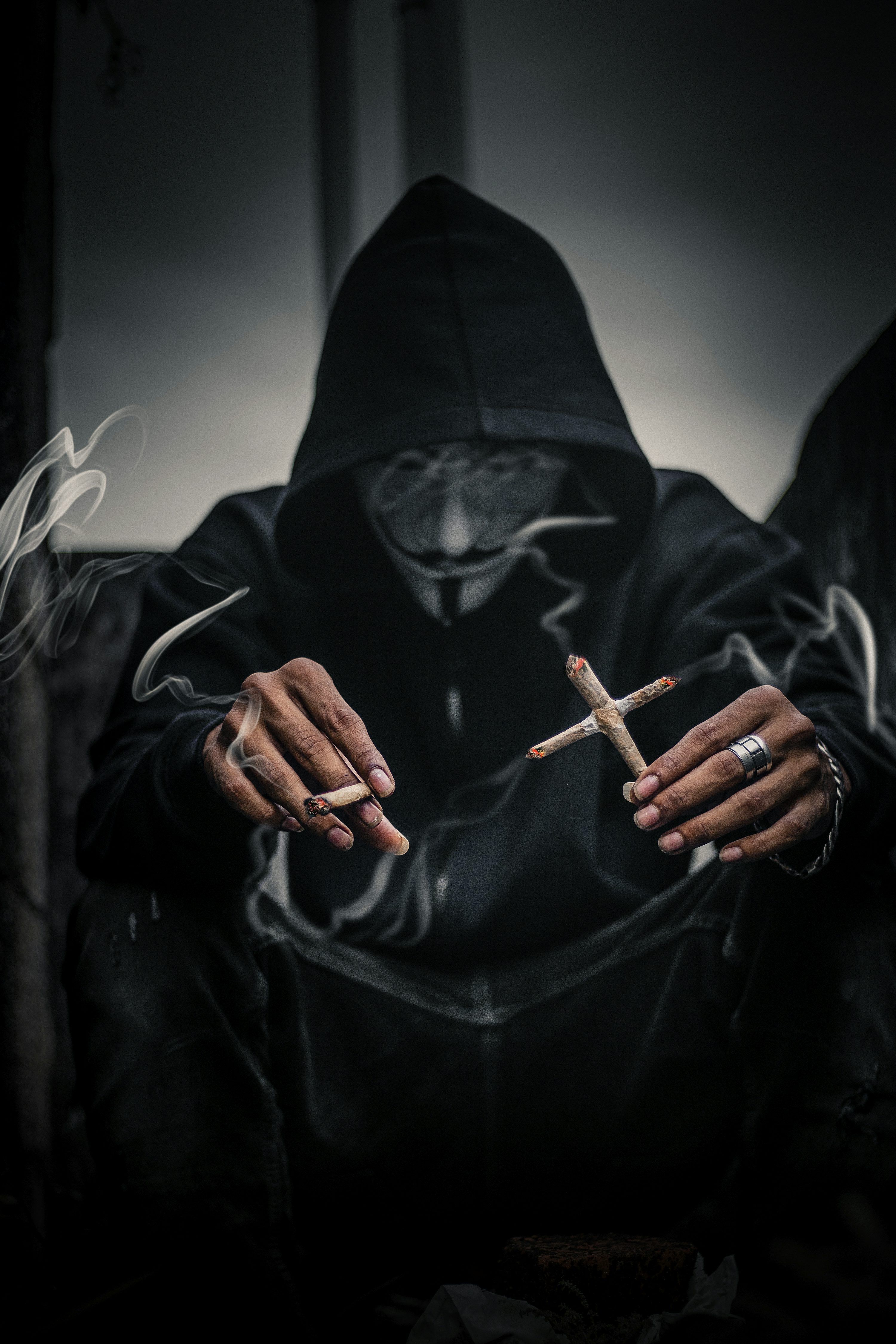 3000x4500 Person In Guy Fawkes Mask Holding Cross Shaped Lighted Cigarettes On His Left With Lighted Joice On Right Hand Photo
