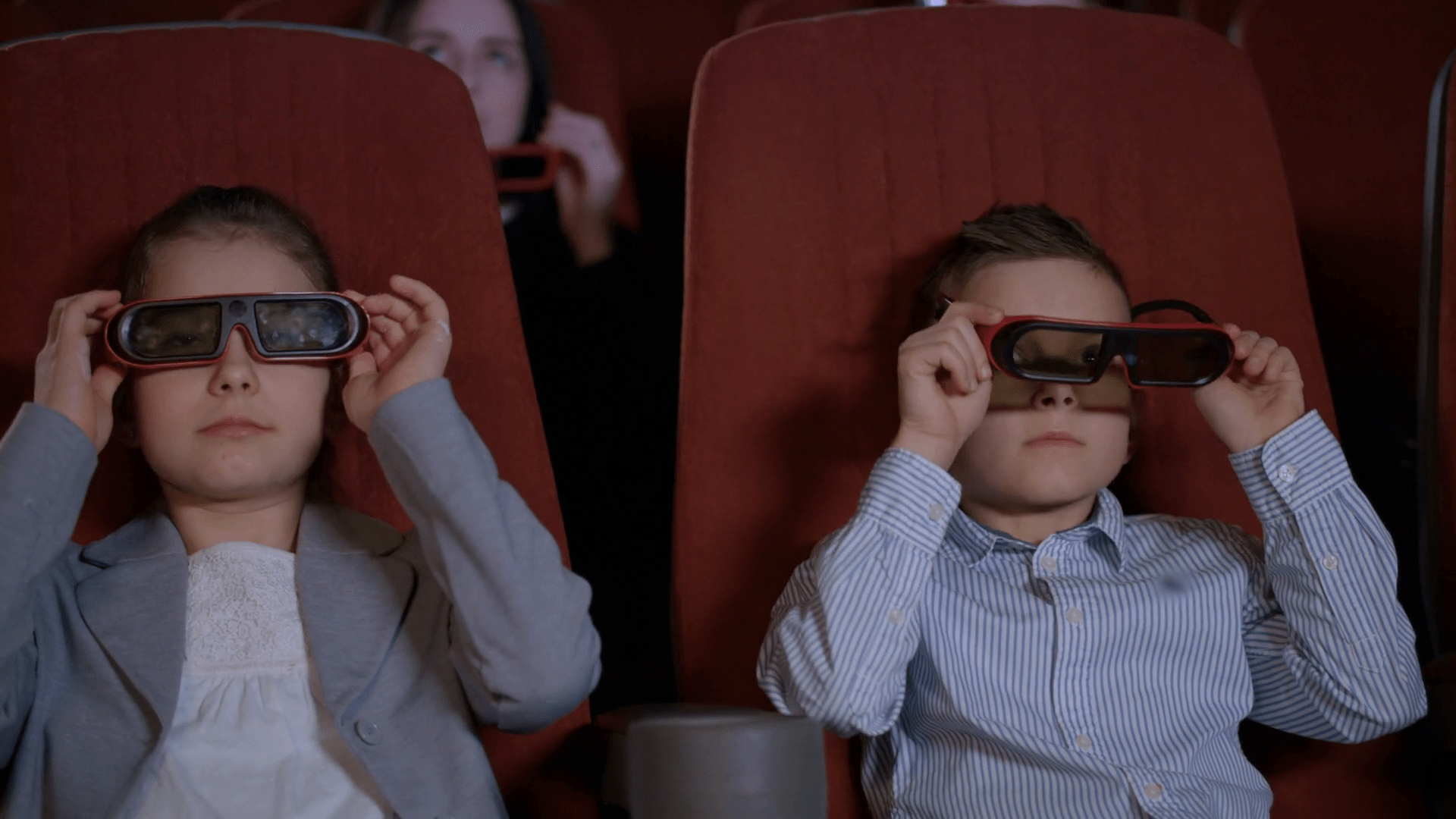 1920x1080 Children wearing 3D glasses at cinema chair. Brother and sister watching 3D film together in slow motion. Boy and girl watching 3D cartoon at movie theater. Modern movie entertainment for kids Stock