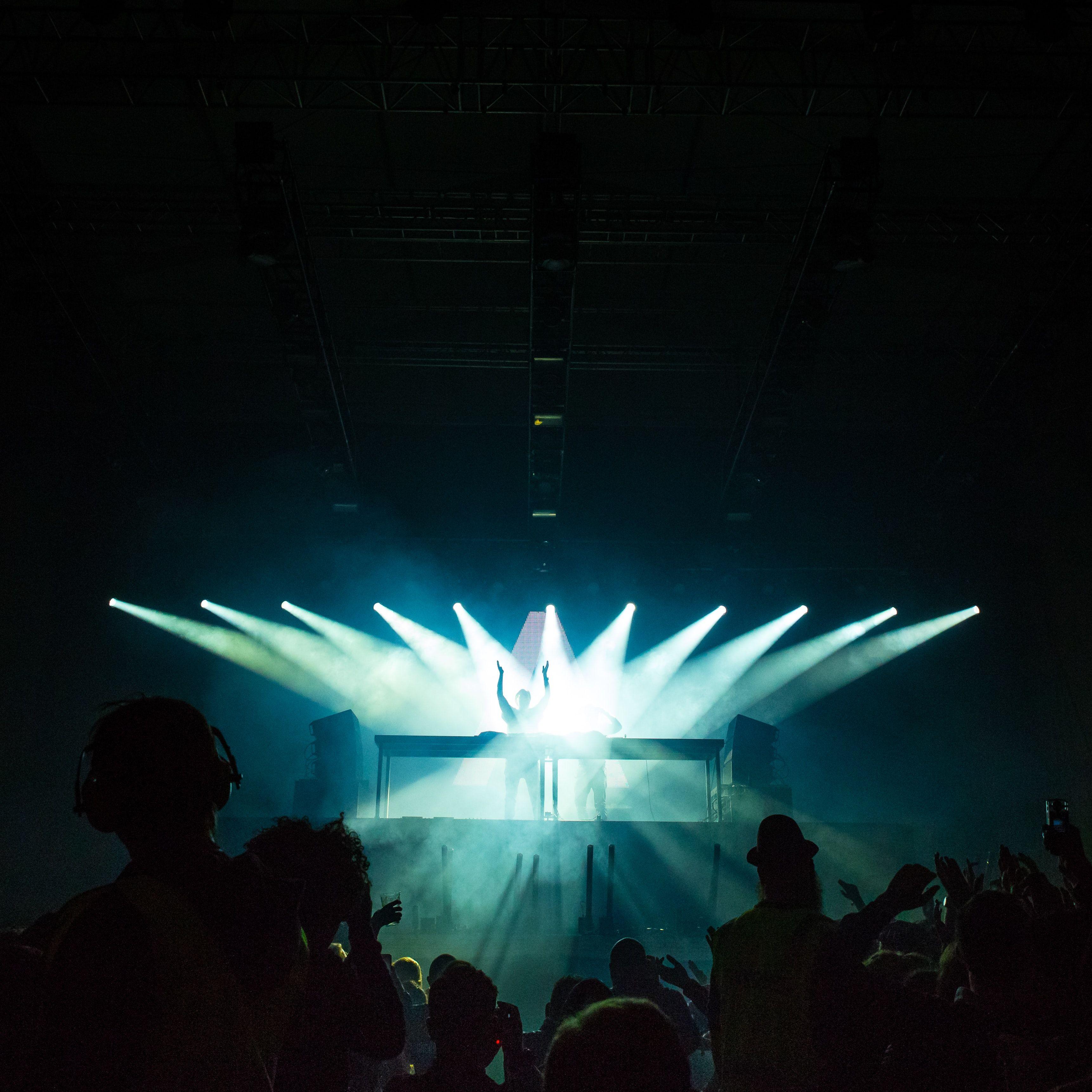 3443x3443 person standing under stage lights facing crowd photo