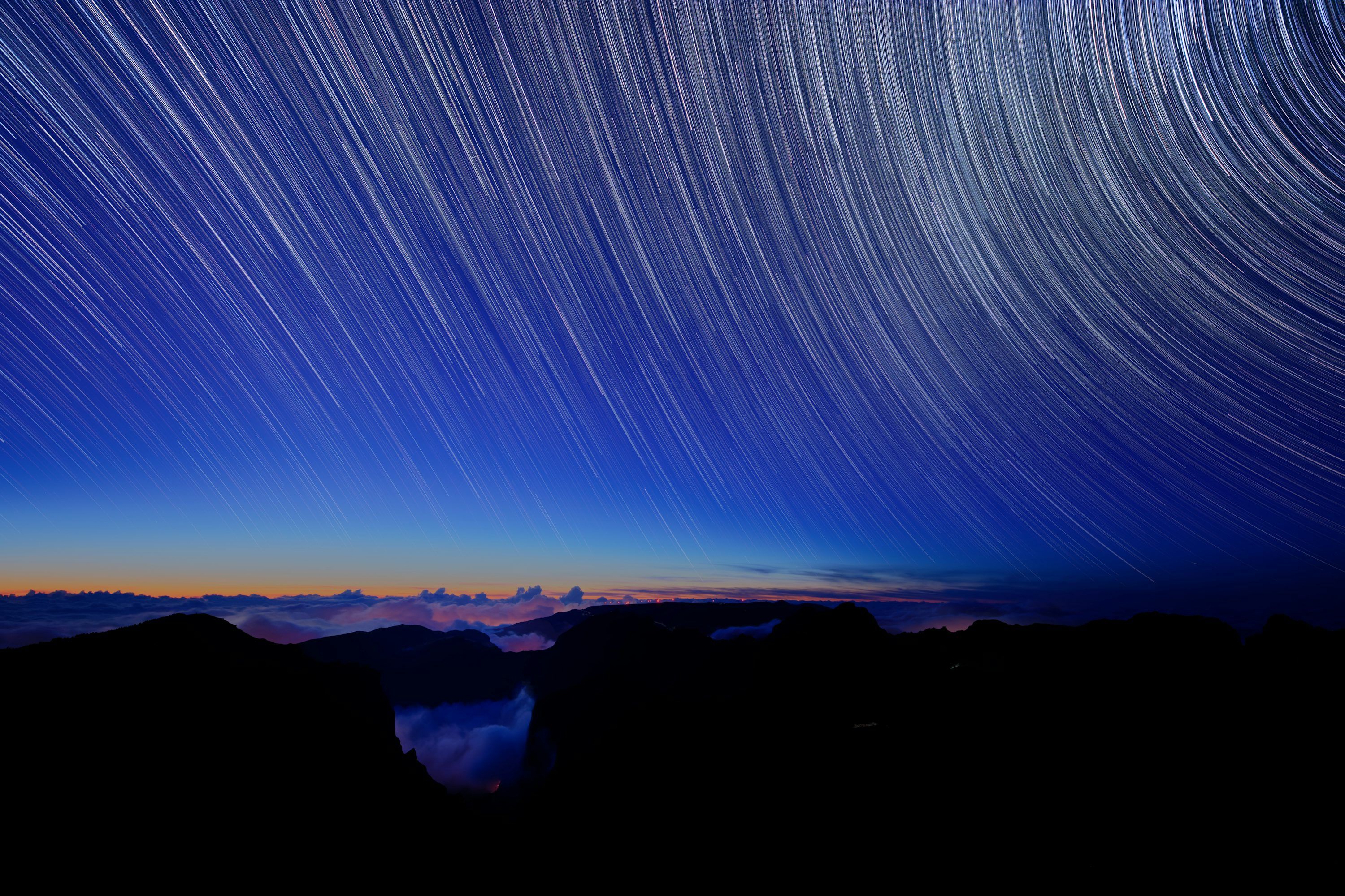 3000x2000 A star trail is seen in the sky above mountains
