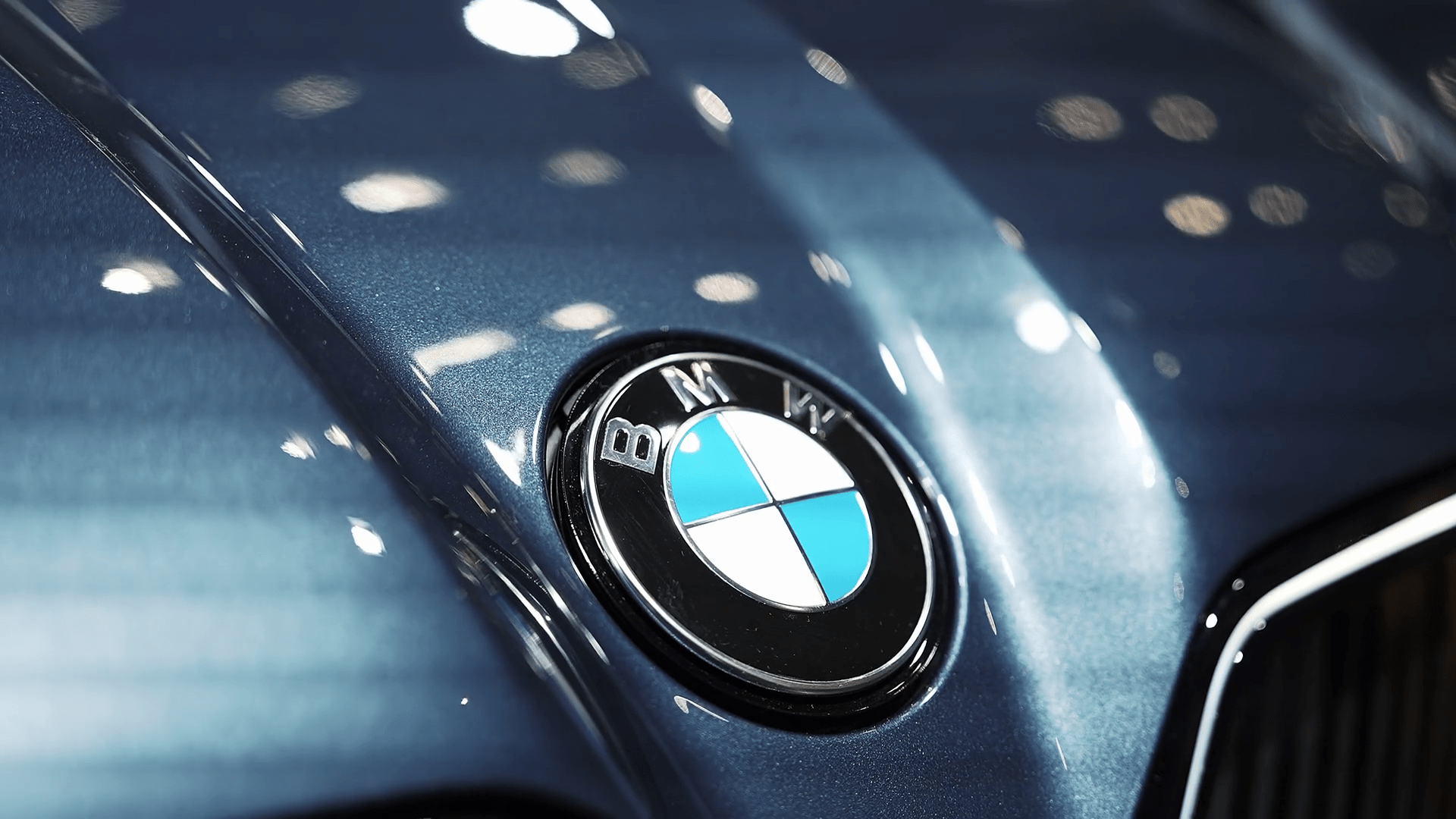1920x1080 A detailed close up of the BMW logo on a glossy metallic blue surface. The static shot highlights the reflective finish and luxury craftsmanship