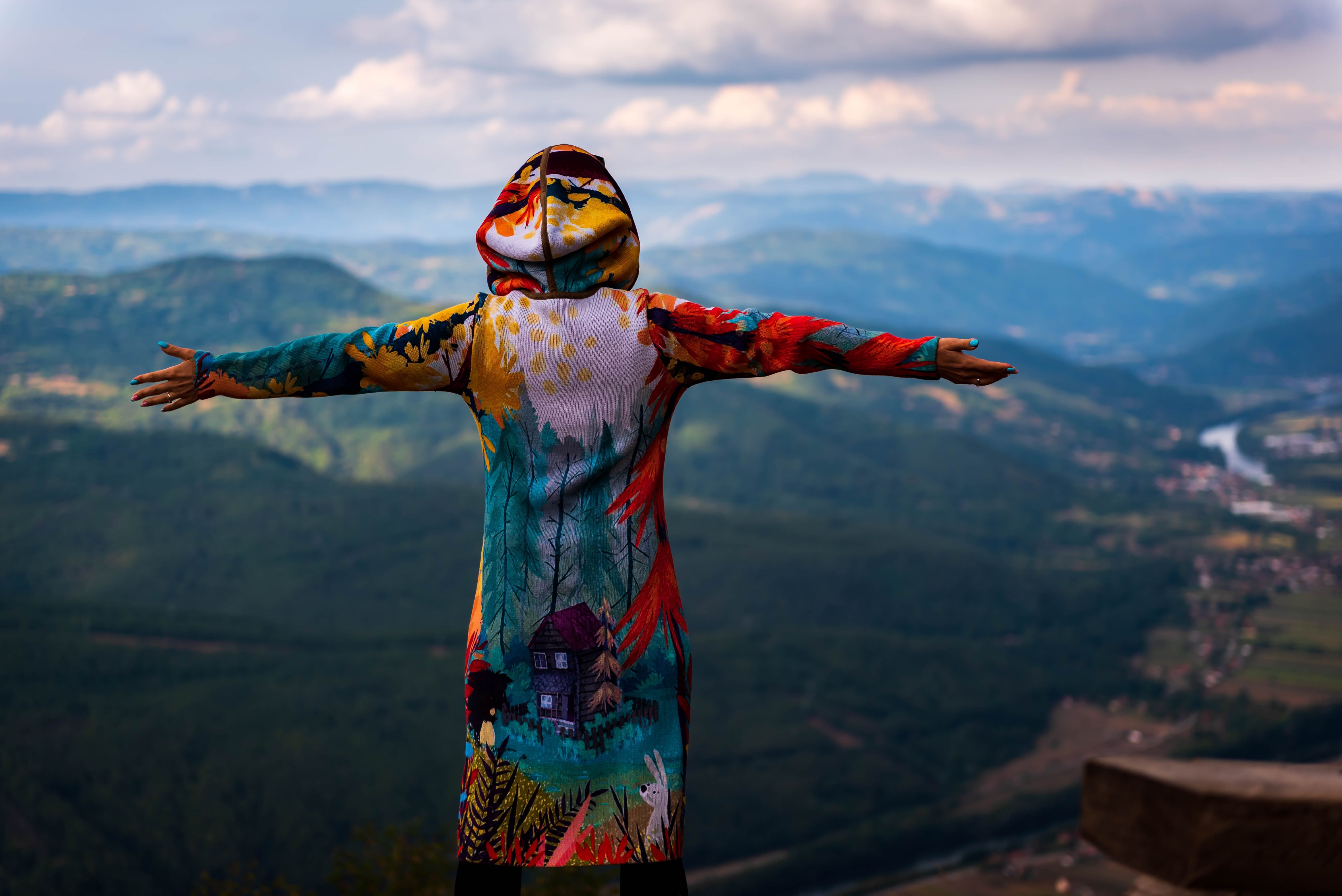 6016x4016 Woman in Colorful Hoodie Standing with Outstretched Arms and Looking at Mountains · Free
