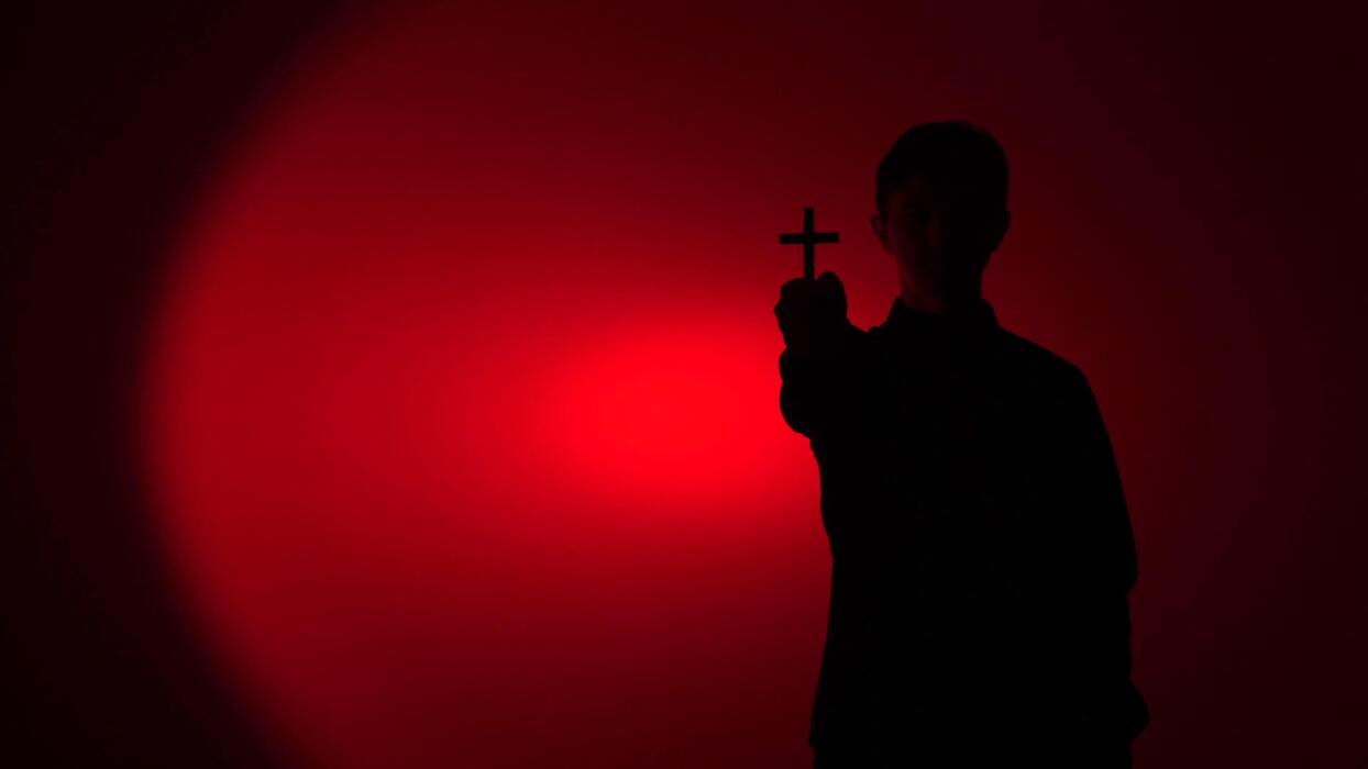 1244x700 Silhouette holding crucifix with spiritual red light, spiritual battle against dark forces