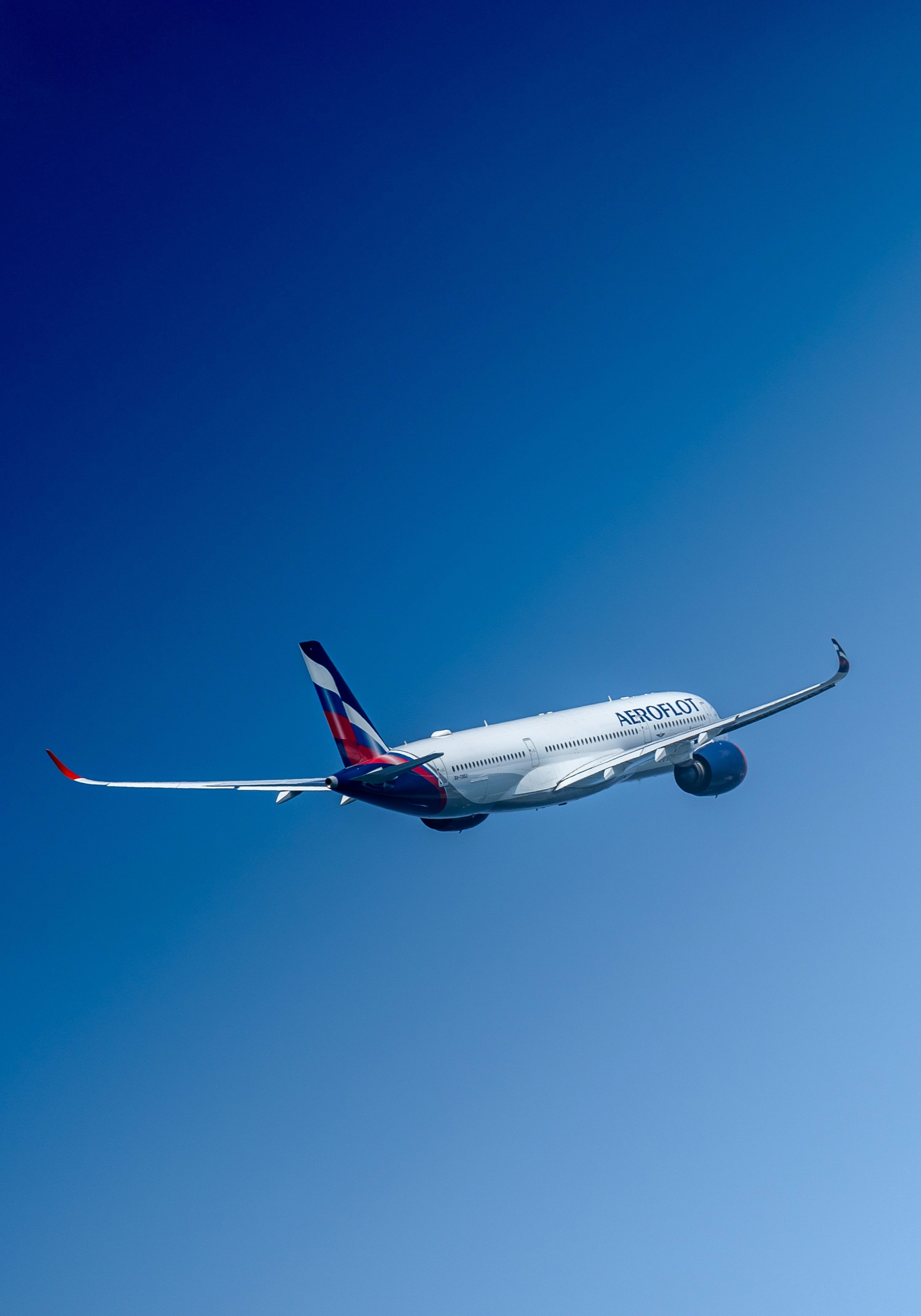 3000x4285 A large commercial airplane flying through a blue sky