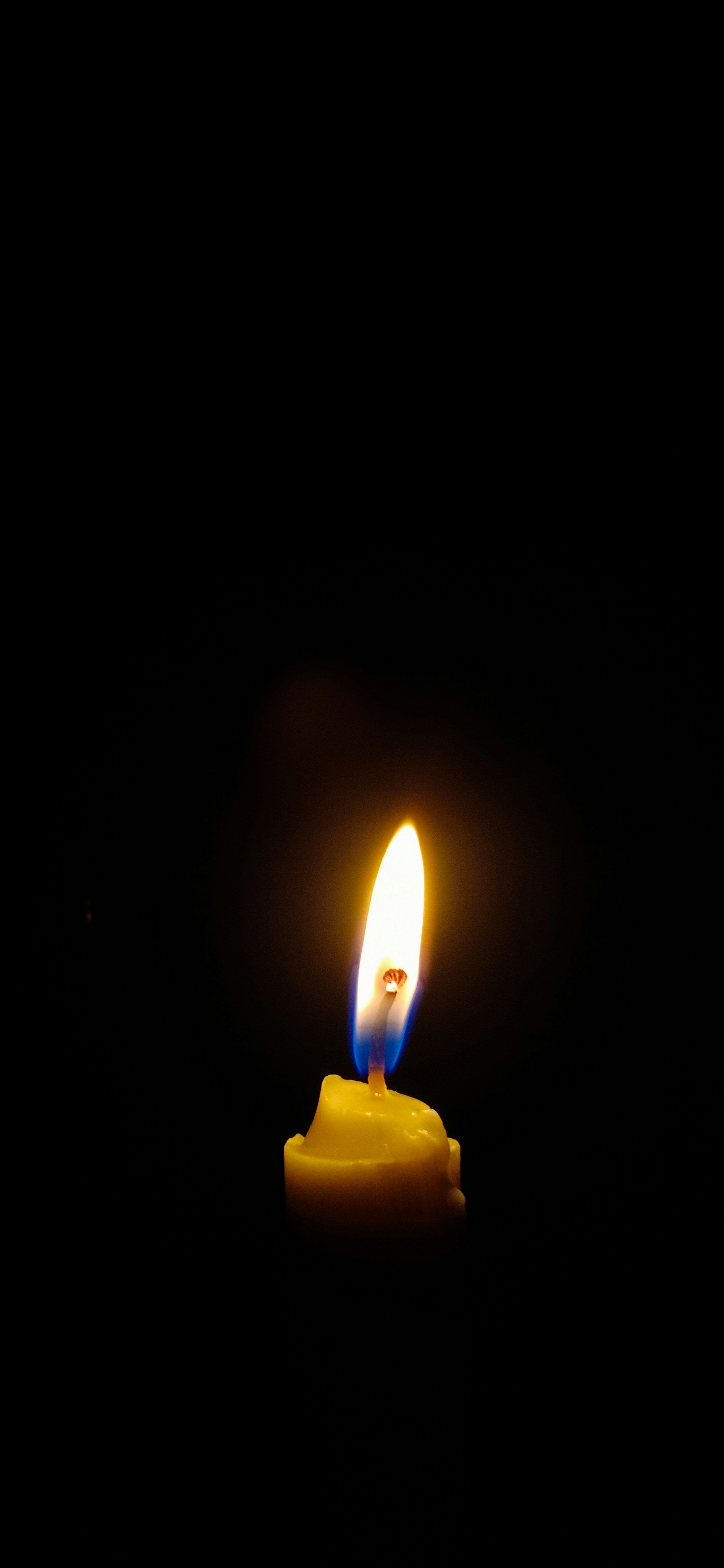 3000x6500 A lit candle in the dark with a black background