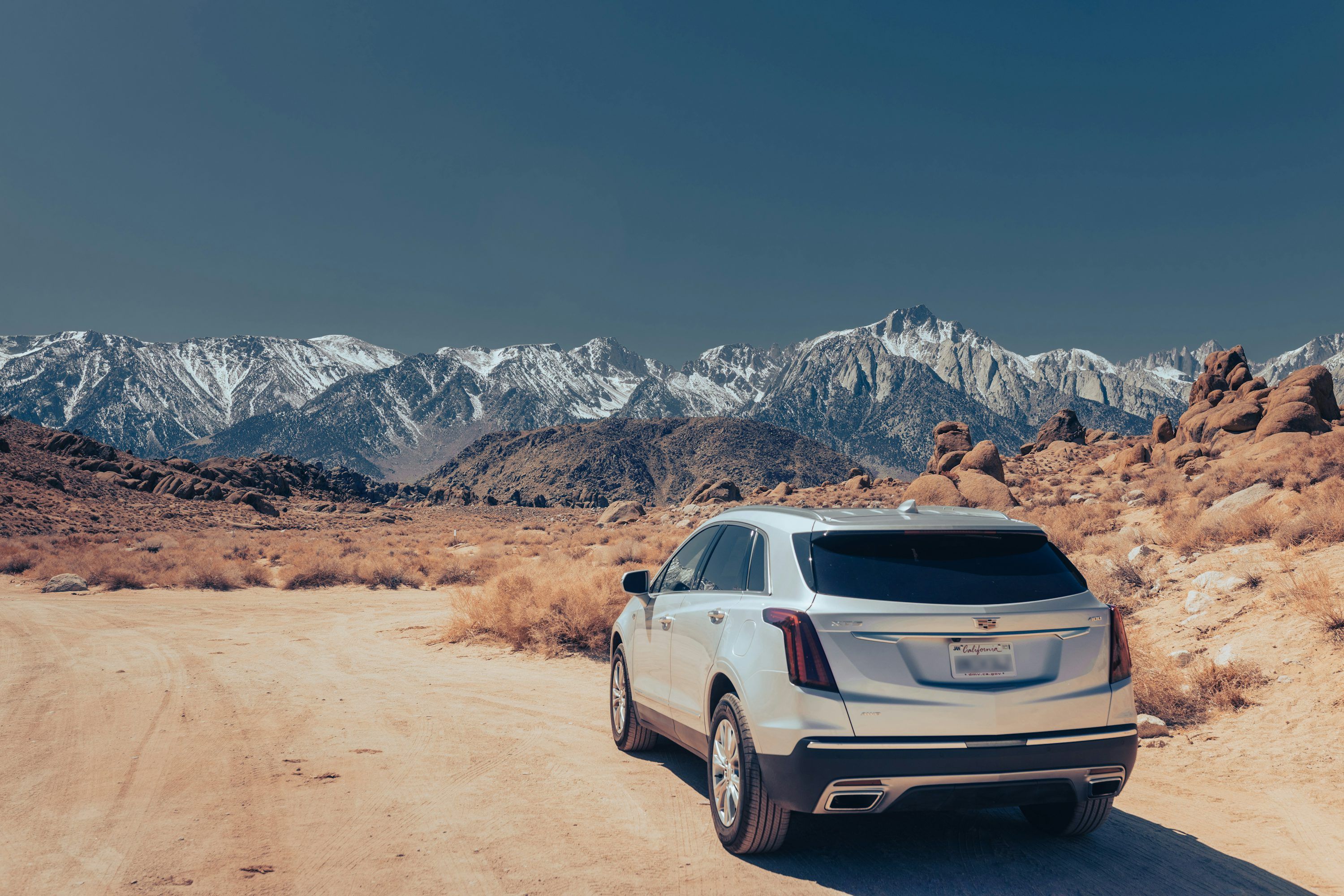 3000x2000 A white cadillac parked on a dirt road in front of mountains