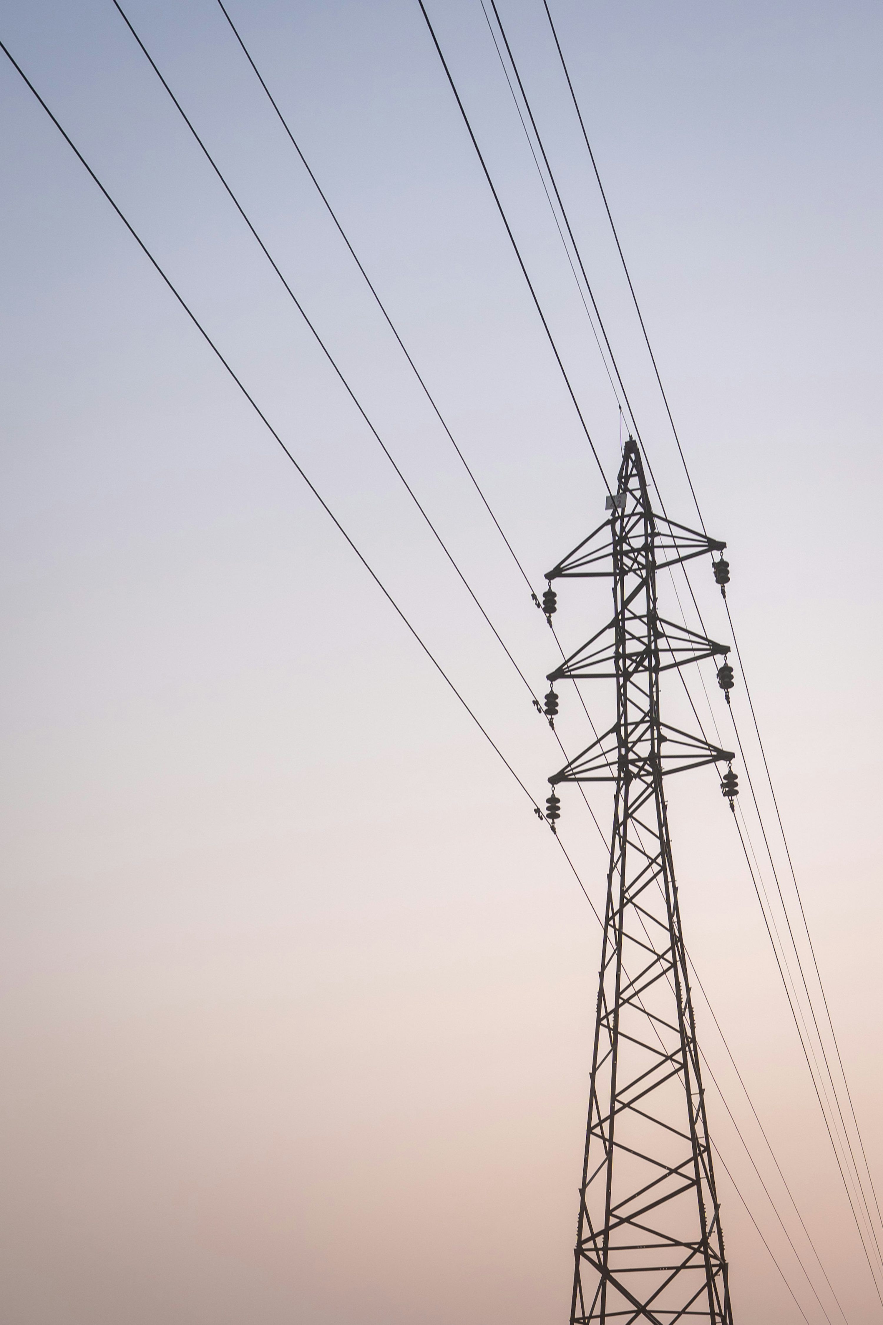 3000x4499 A tall electricity pylon stands against a soft gradient sky