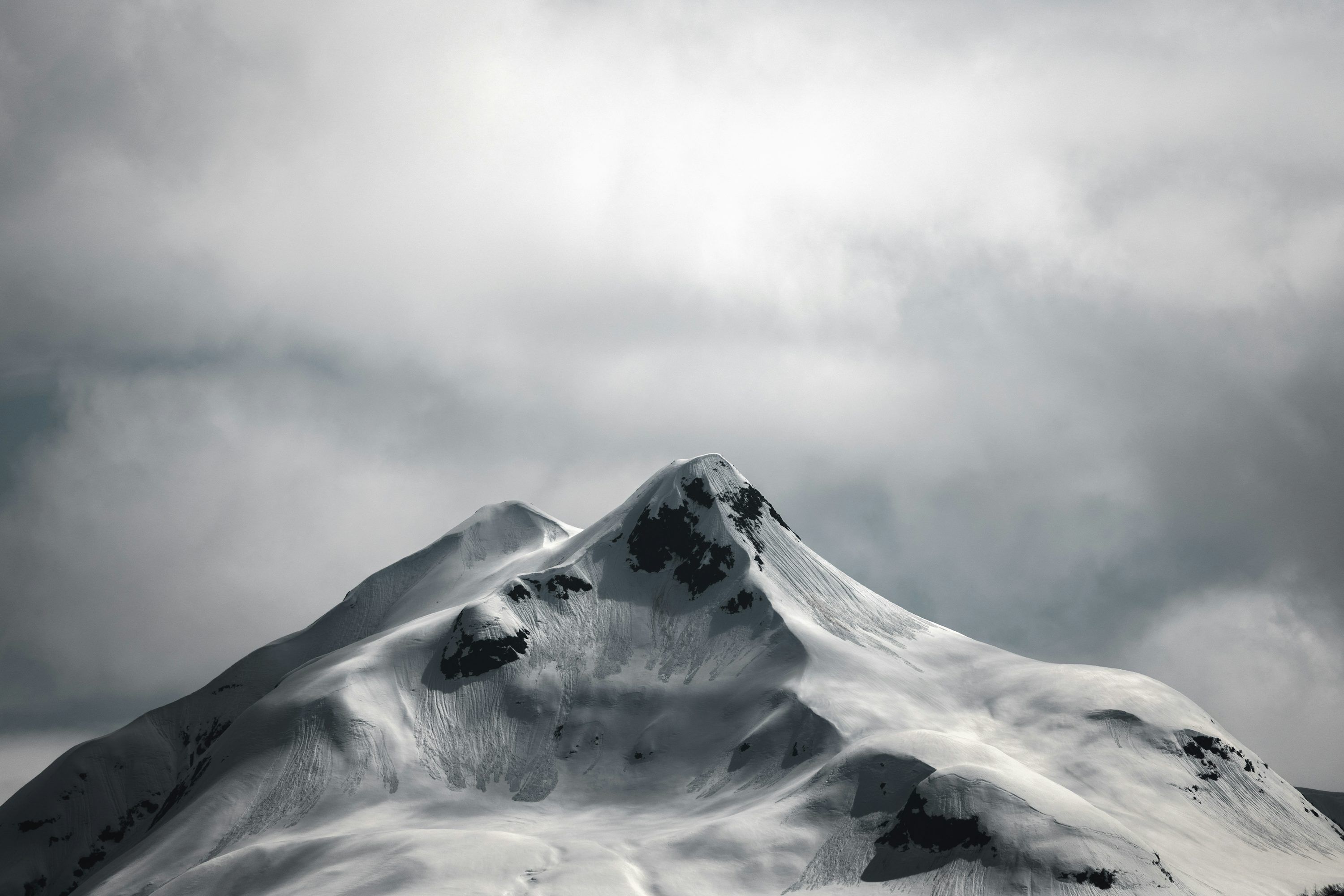 3000x2000 A Snow Covered Mountain Peak Under A Dramatic Cloudy Sky