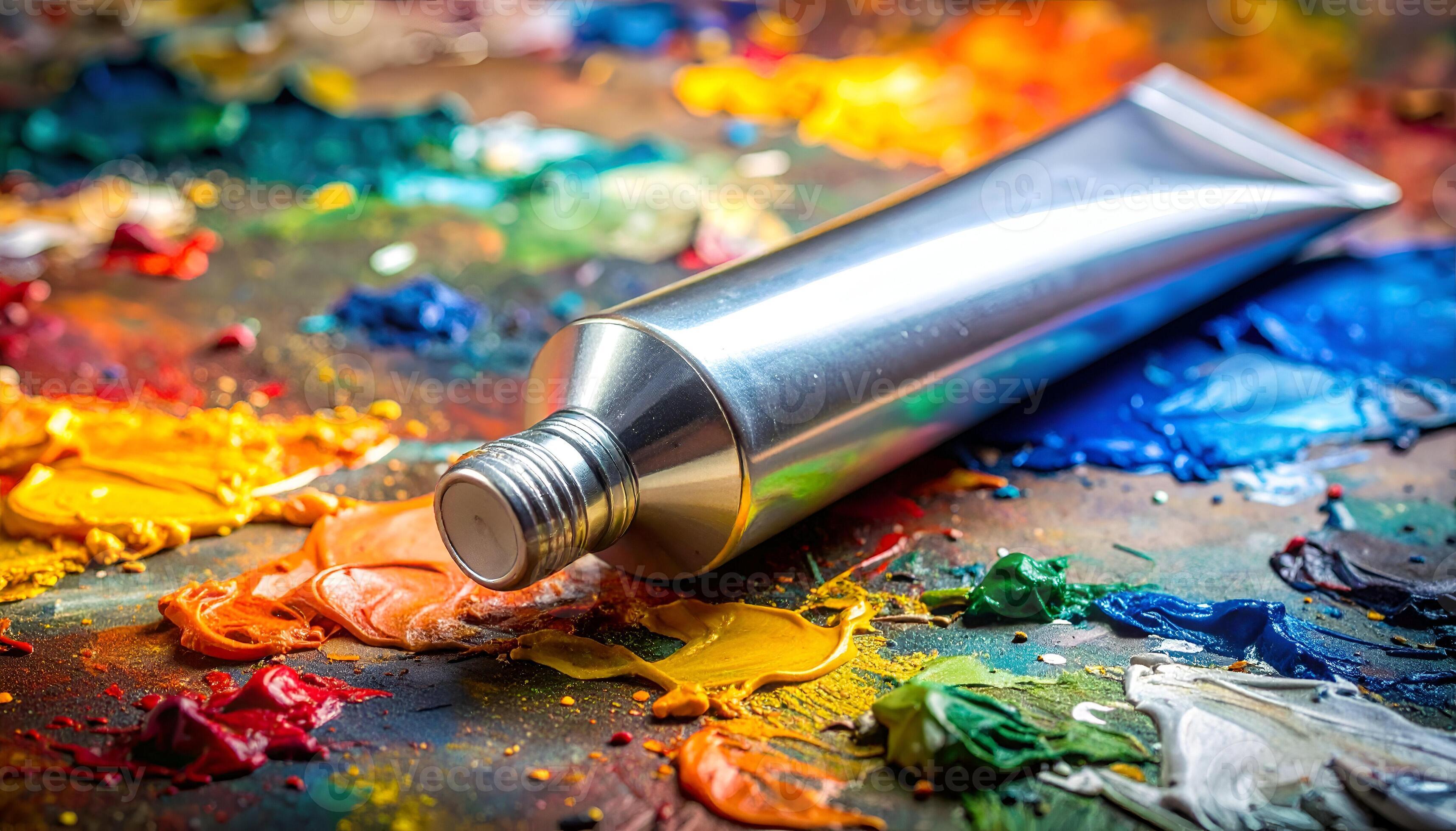3430x1960 Silver paint tube resting on a vibrant, messy artist's palette with thick splatters of bright oil and acrylic colors