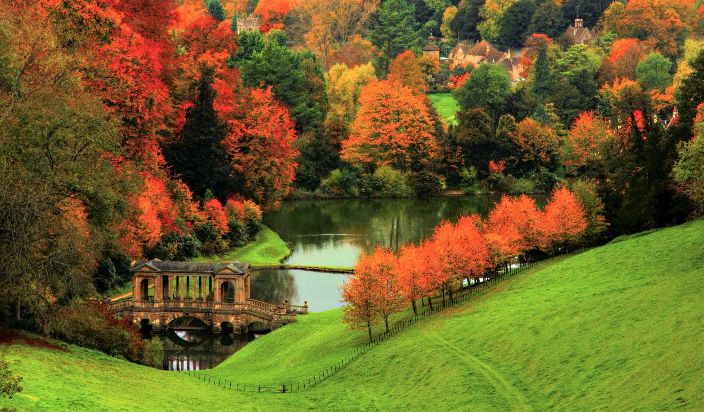 2900x1698 Autumn Splendor: Vibrant Forest Bridge & Lakeside Town HD Wallpaperx1698