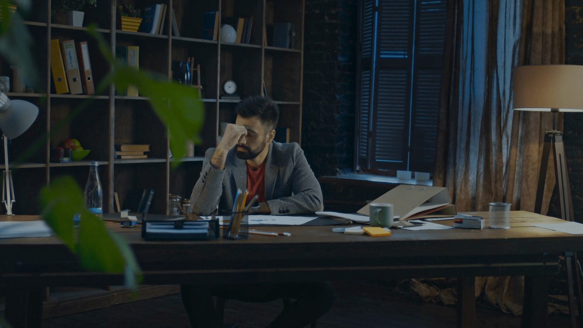 1920x1080 Tired businessman at end of work day in home studio. Disappointed business man put hands on head at table in evening. Upset businessman working in cozy office. Business hard work in stress