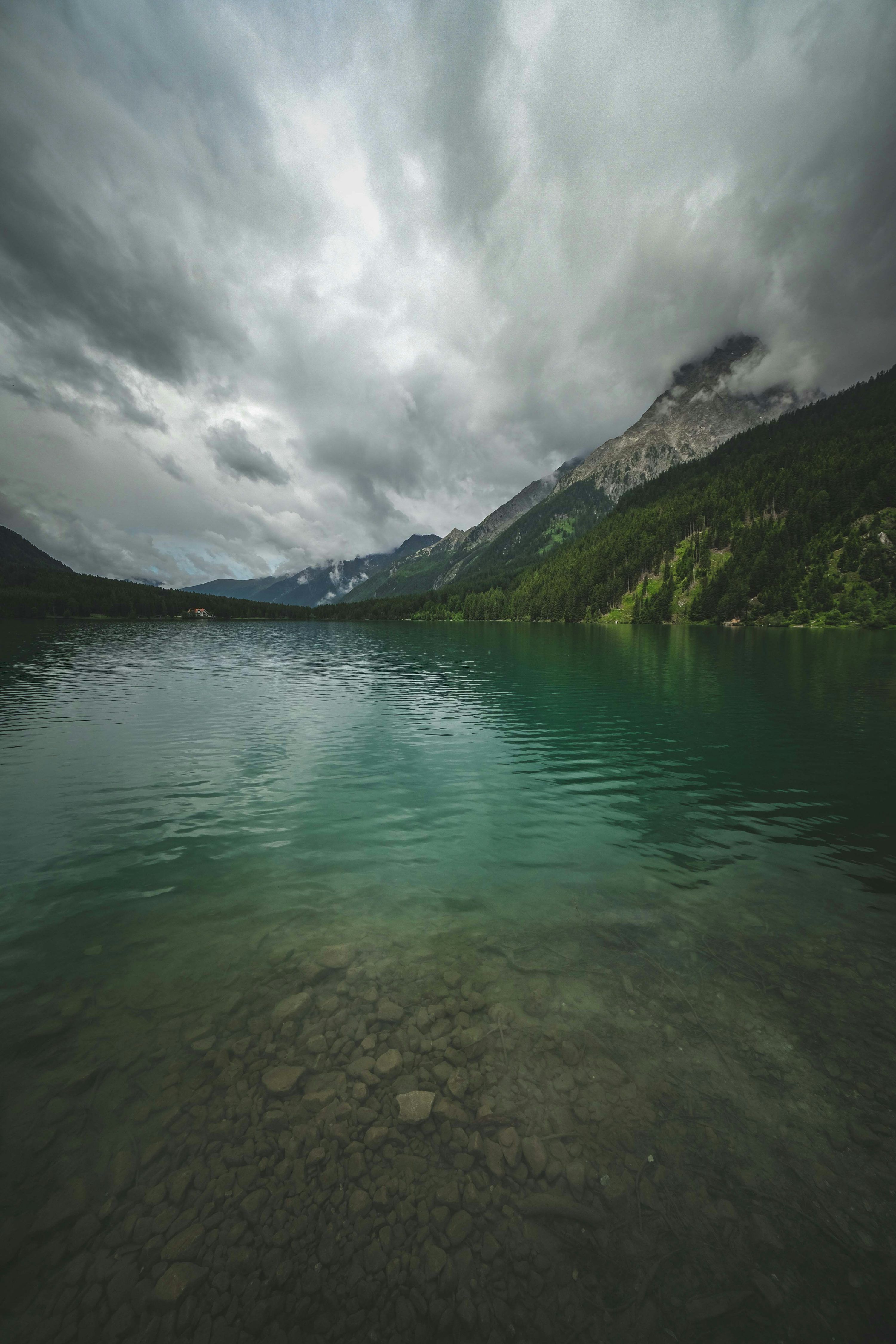 3000x4500 A body of water surrounded by mountains under a cloudy sky