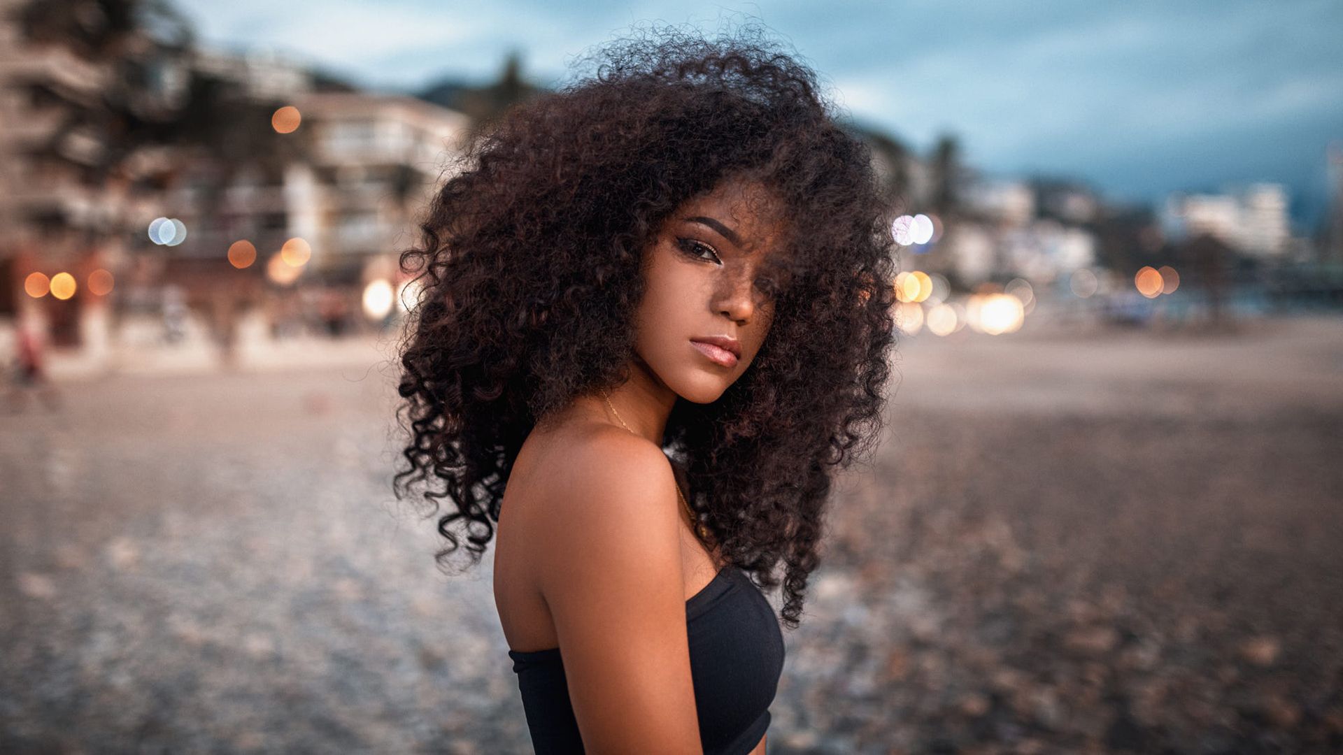 1920x1080 Curly Hair Girl Model Is Standing In Blur Bokeh Background Wearing Black Dress HD Girls Wallpaper