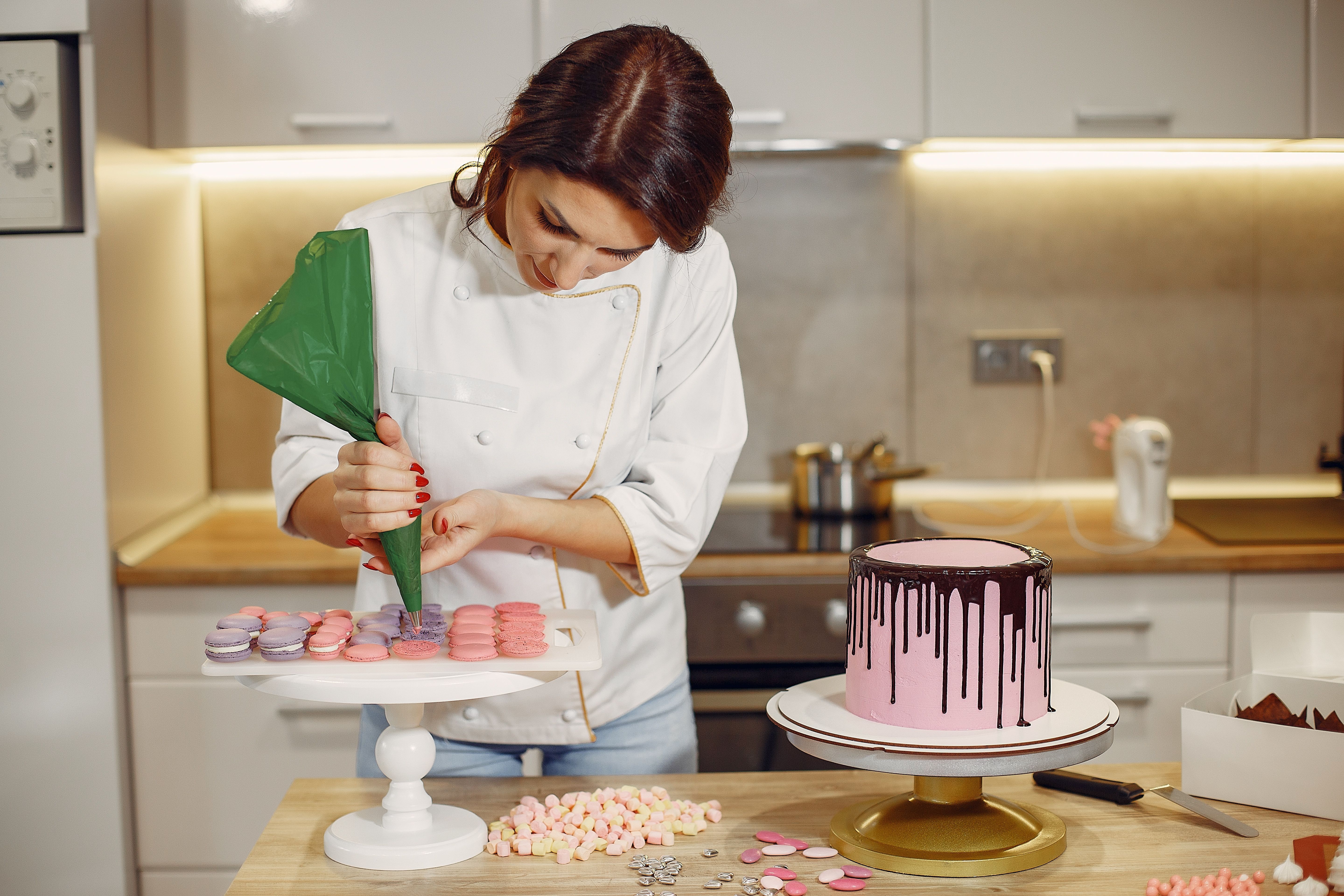 5760x3840 Female pastry chef adding cream on macaroons shells in modern bakery · Free