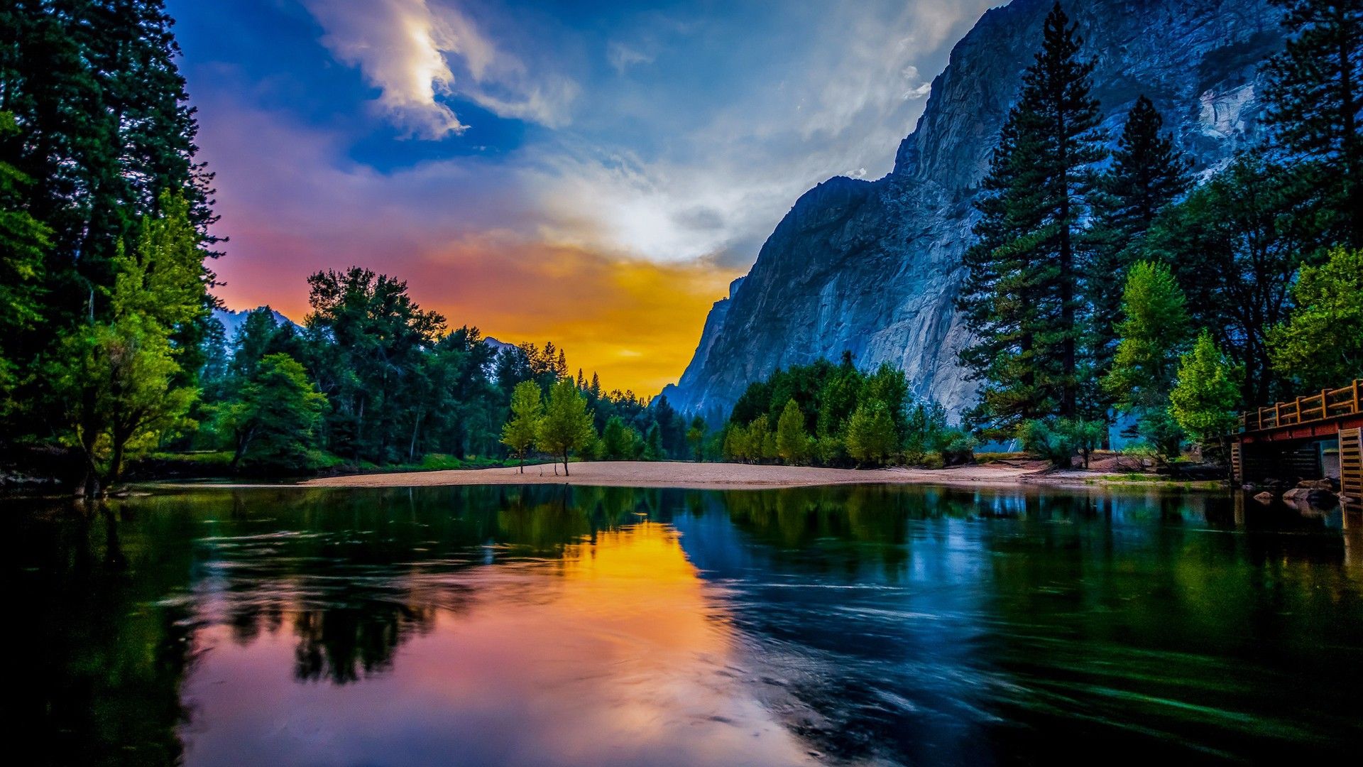 1920x1080 River Between Green Trees And Mountains Reflection On Water In Yellow White Clouds Blue Sky Background HD Nature Wallpaper