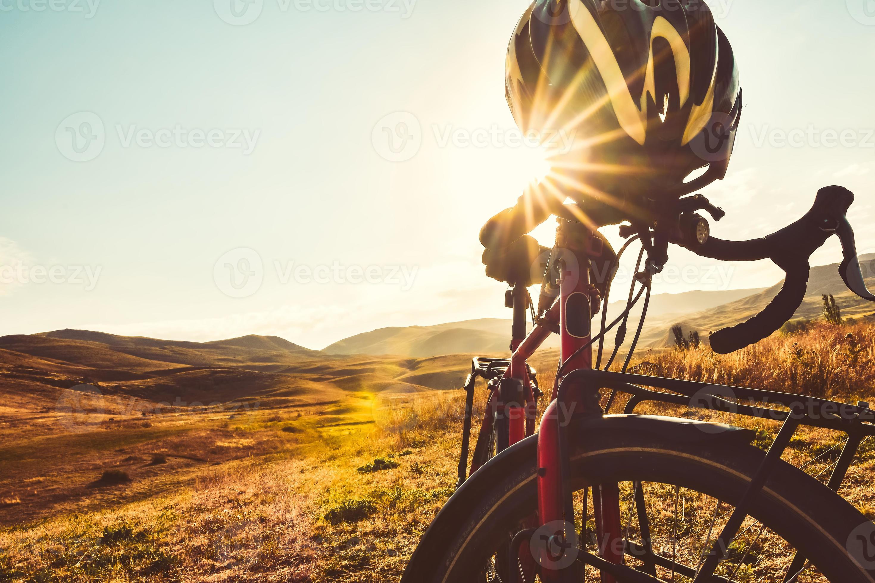 2940x1960 Close up bicycle stand in nature with sunflare peaks through helmet. Cinematic cycle wallpaper. Travel transport red bike