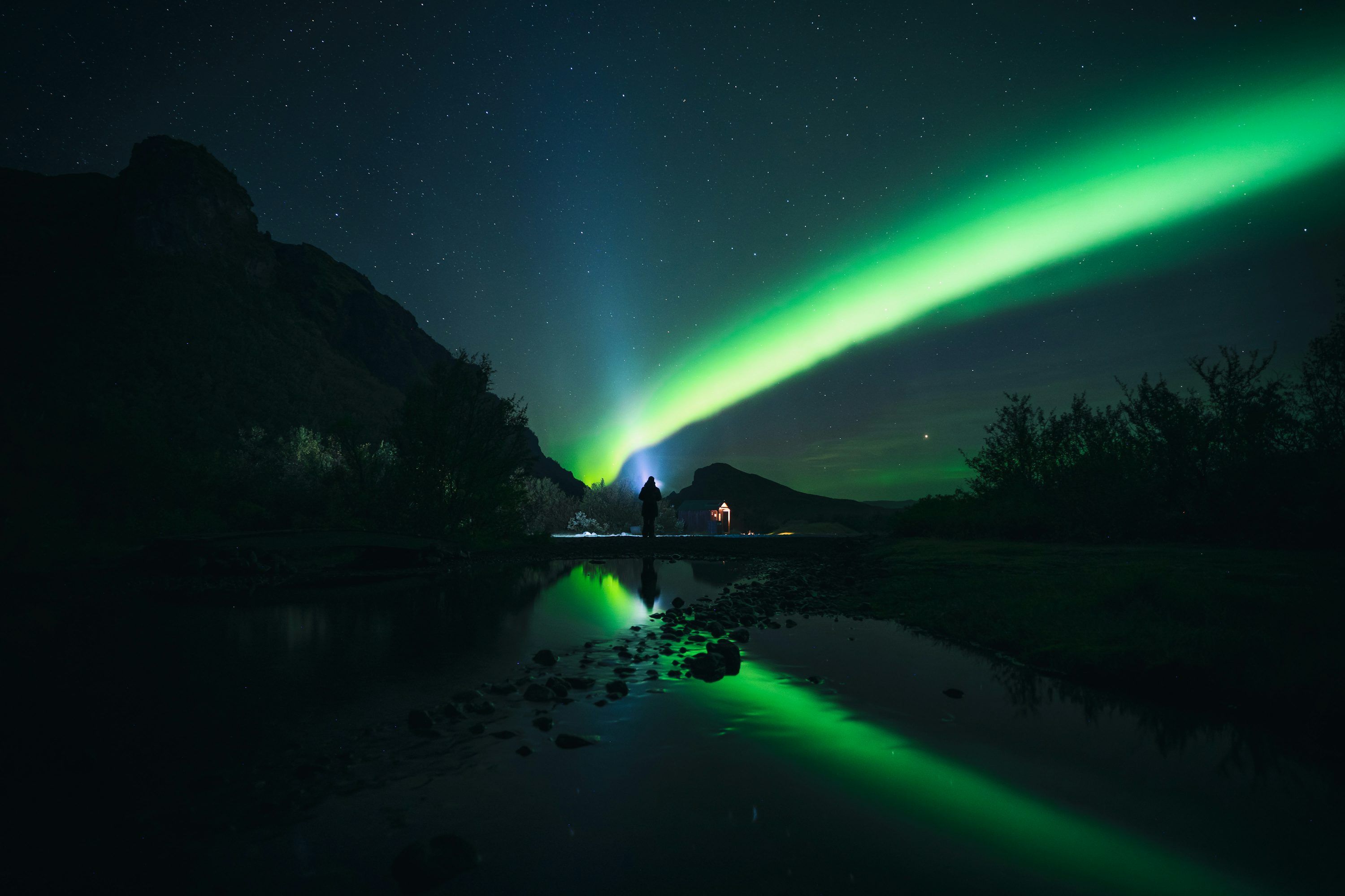 3000x2000 A body of water with a bright green light in the sky above
