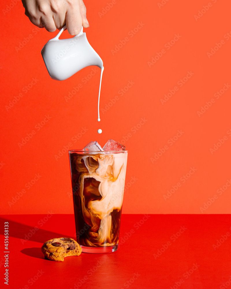 800x1000 Iced coffee on a bright red background with a hand pouring cream into the coffee Wall Mural. Buy online at