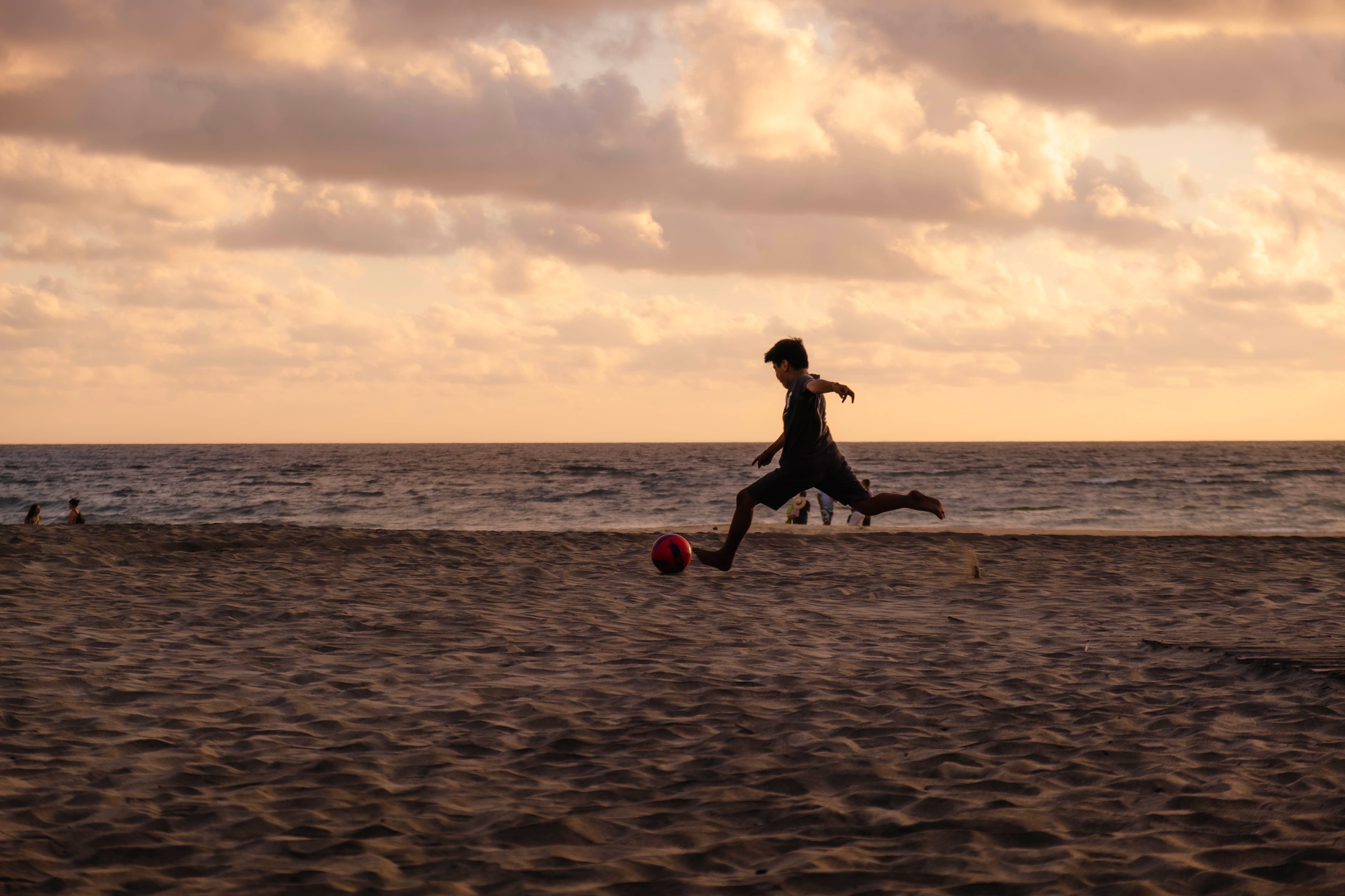 6240x4160 Young Boy Playing Football on Beach · Free