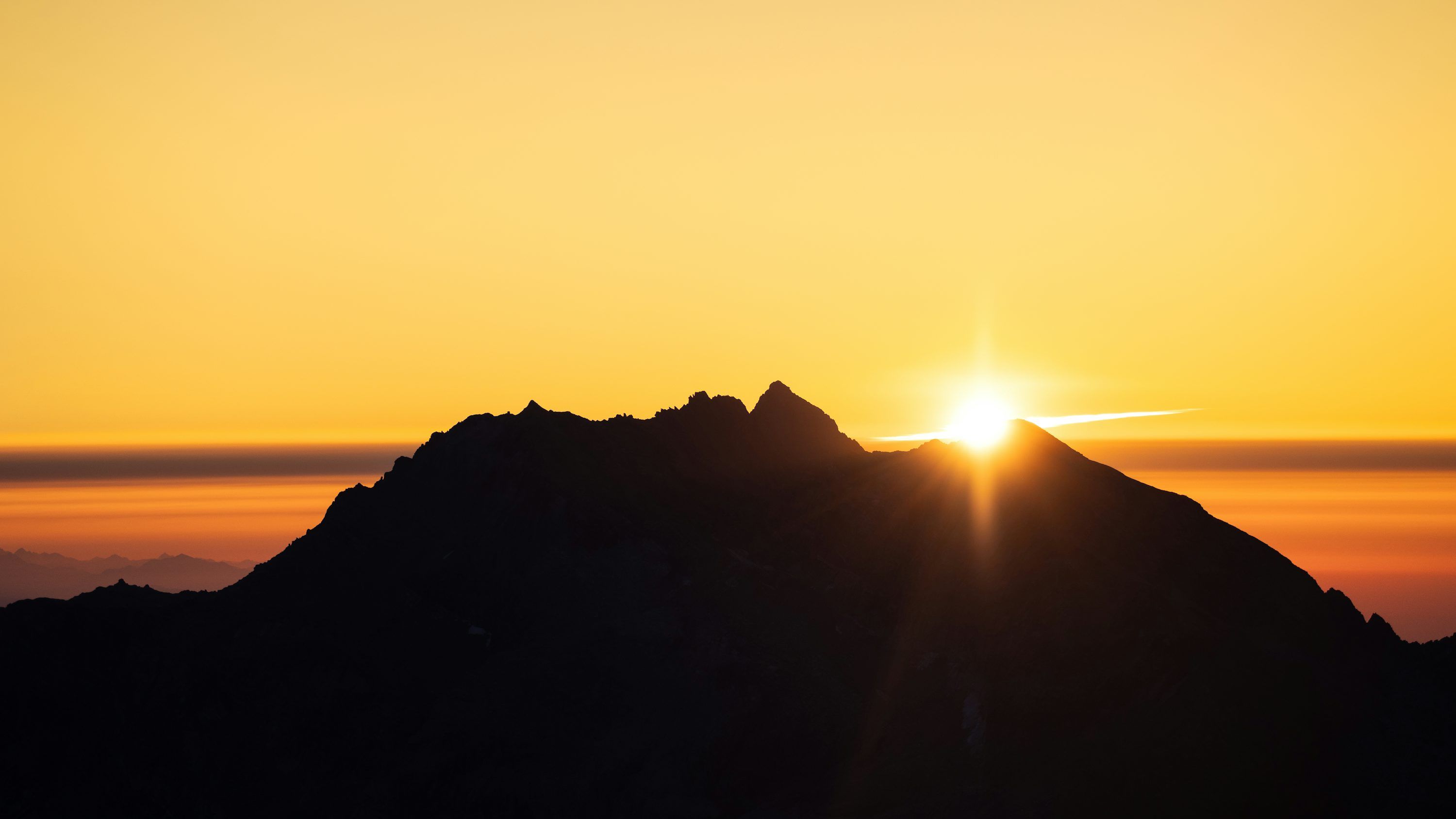 3000x1688 Sunrise peaks over a mountain silhouette