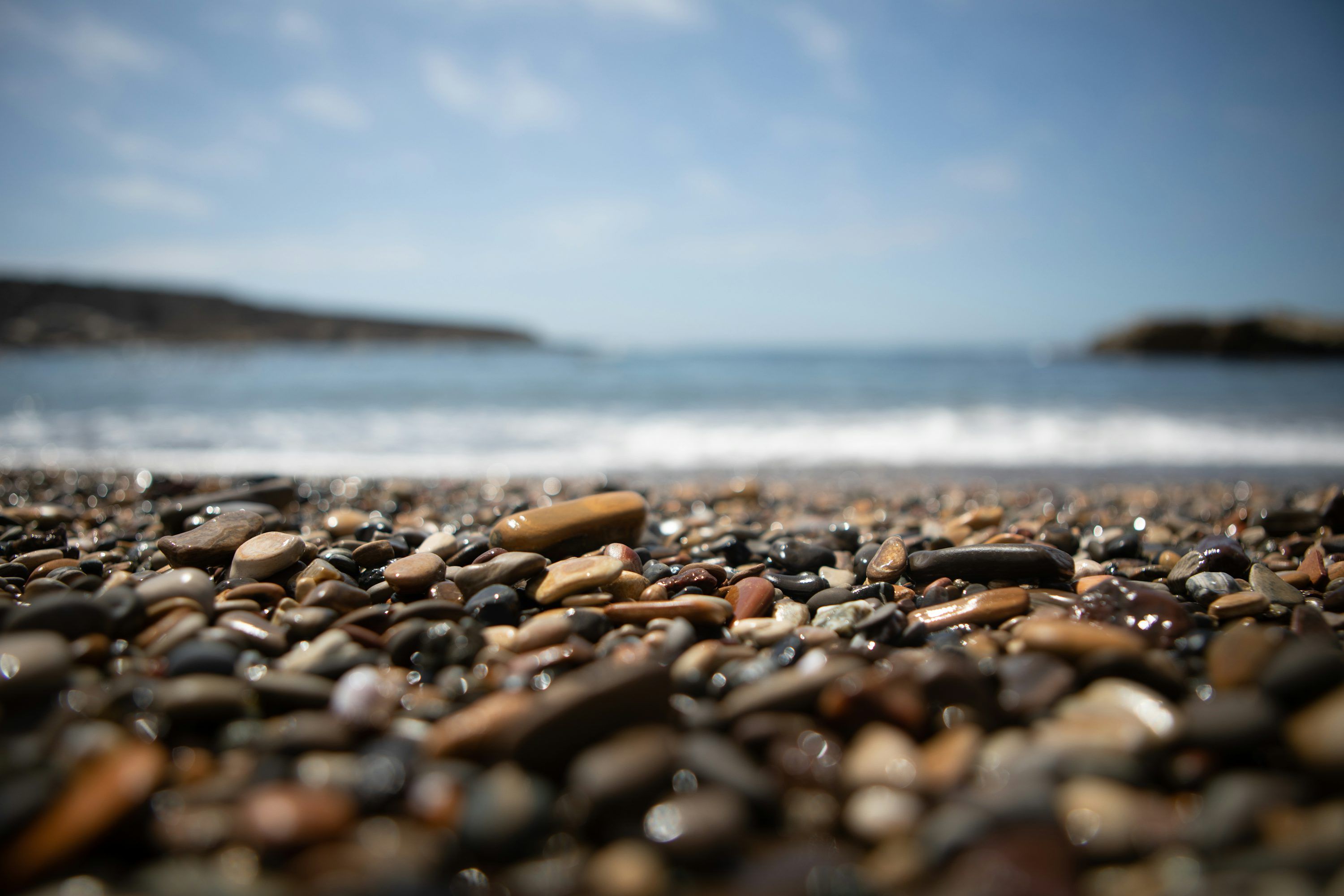 3000x2000 A close up of rocks on a beach with a body of water in the background