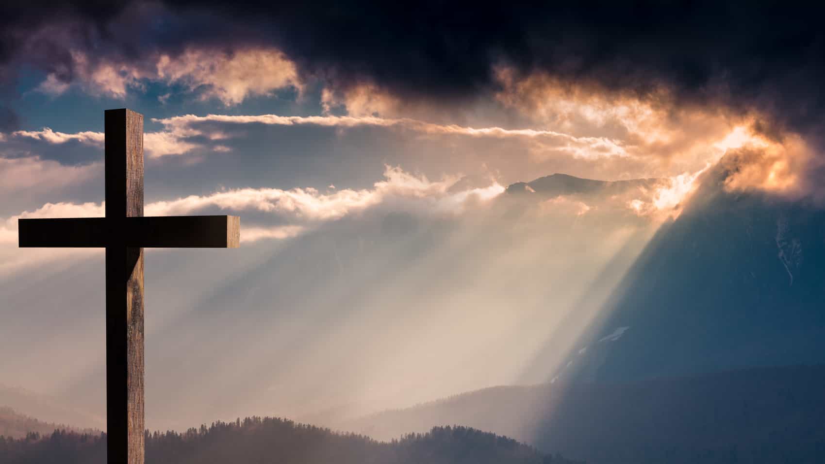1700x956 Jesus Christ cross. Easter, resurrection concept. Christian cross on a background with dramatic lighting, colorful mountain sunset, dark clouds and sky and sunbeams Savior's Lutheran Church