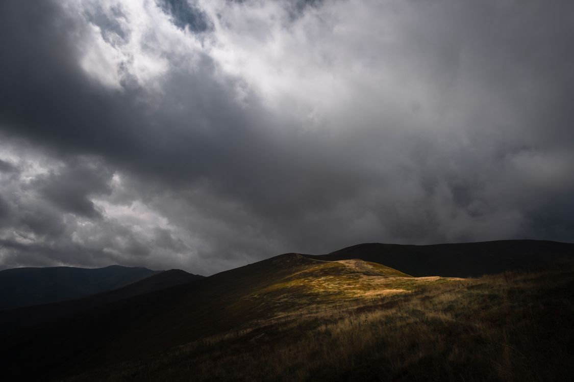 1125x750 A dark stormy sky over a hill with grass and trees · Free