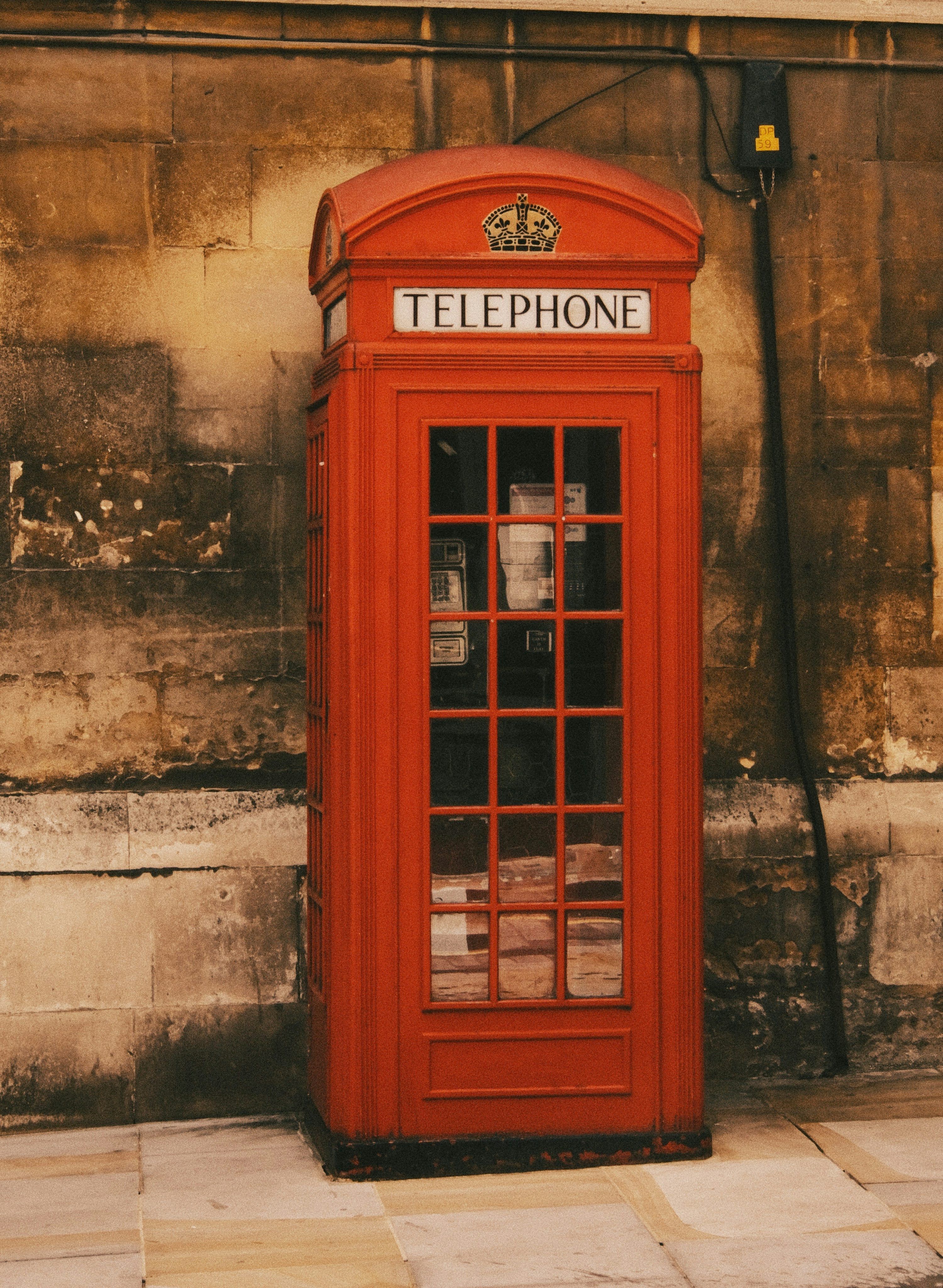 3000x4097 A red telephone booth sitting on the side of a building