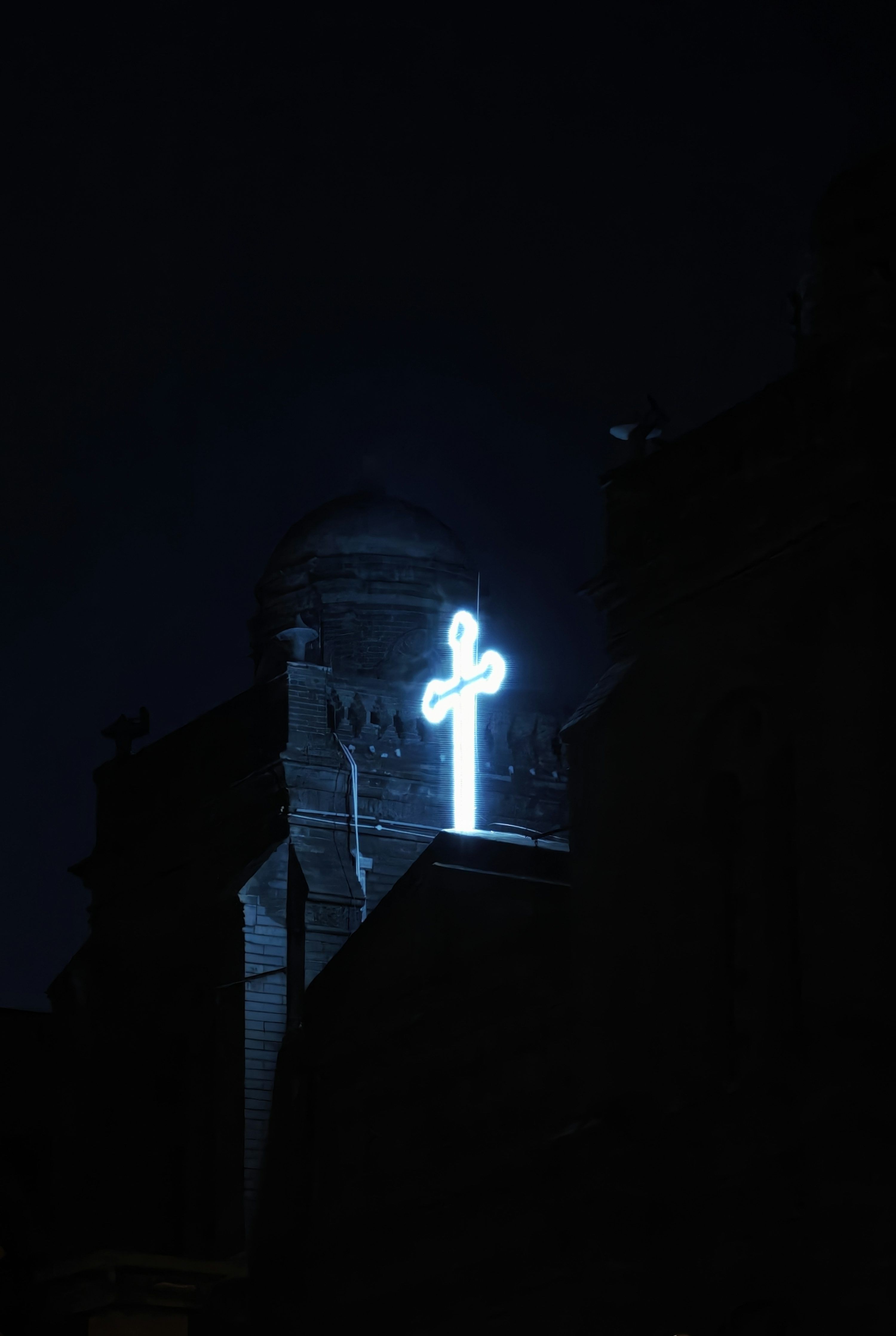3000x4470 A glowing neon cross atop a building at night
