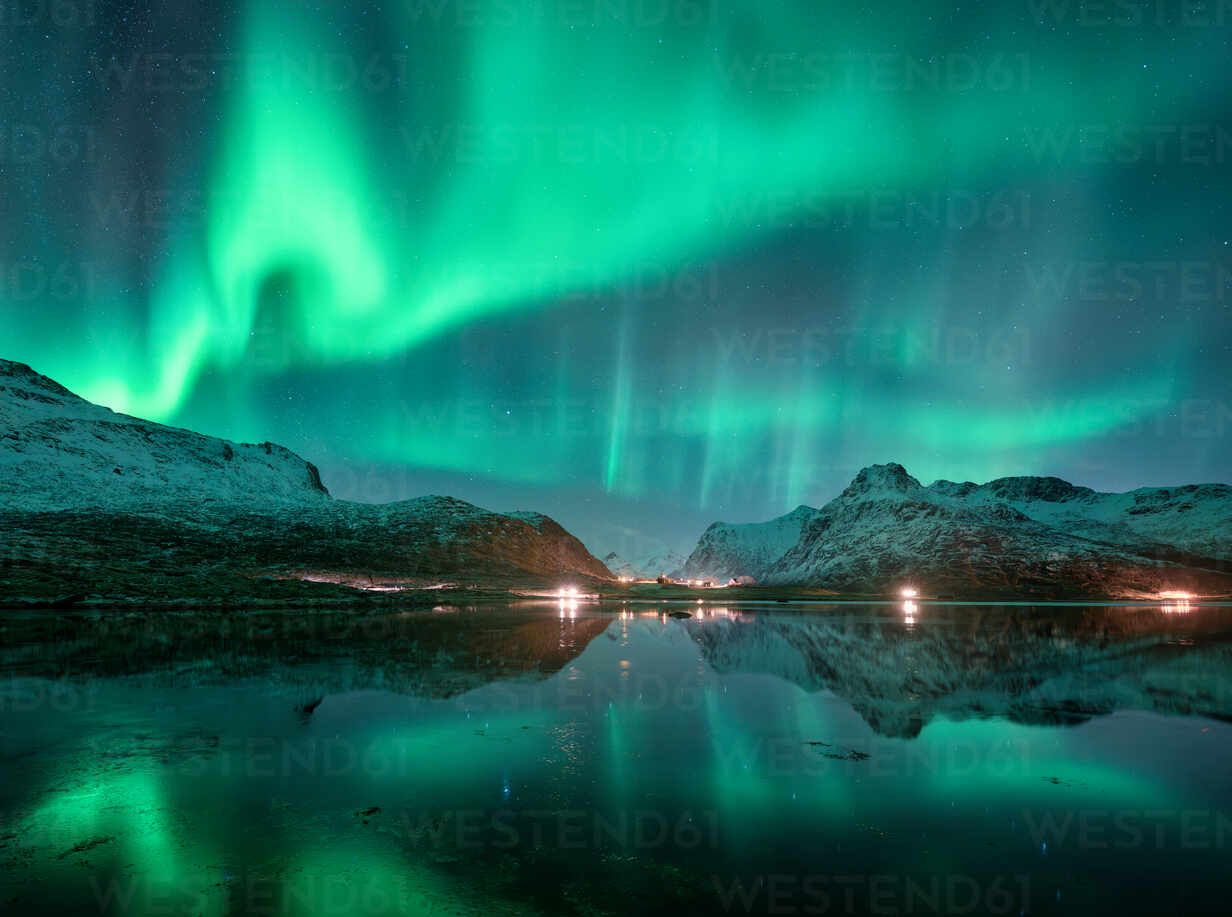 1232x917 Aurora borealis over snowy mountains and calm reflective lake. Bright green Northern lights illuminate the winter landscape at night with clear sky in Lofoten Islands, Norway. Landscape with Aurora