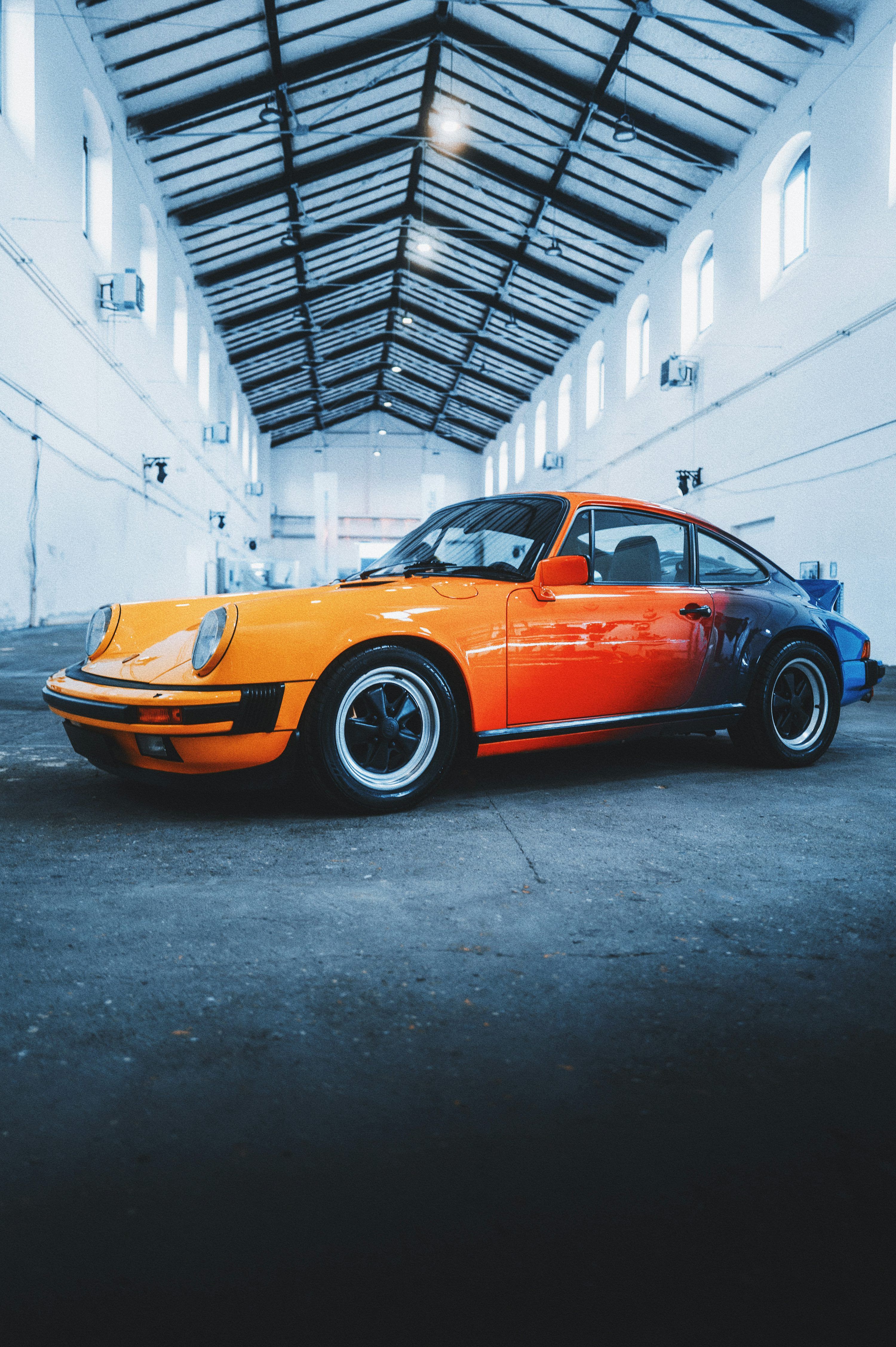3000x4507 An orange and blue porsche parked in a garage