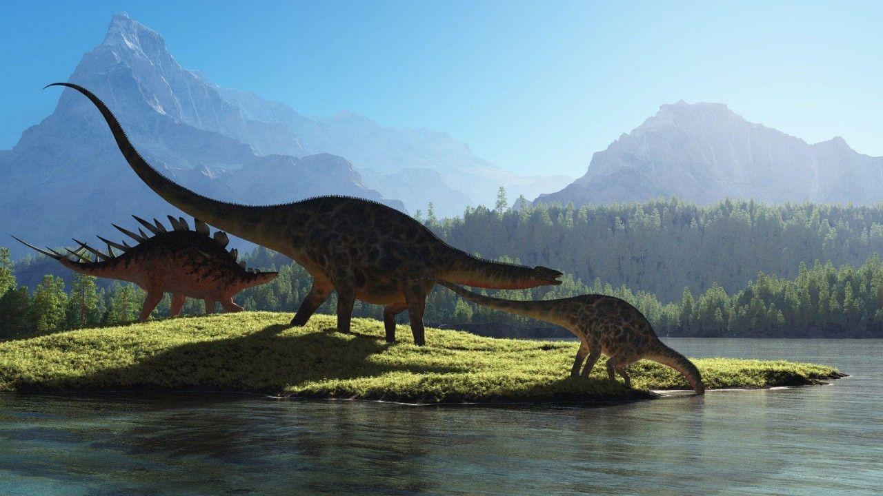 1280x720 Dinosaurs Are On Grass Field Drinking Water With Mountain And Blue Sky Background HD Dinosaur Wallpaper