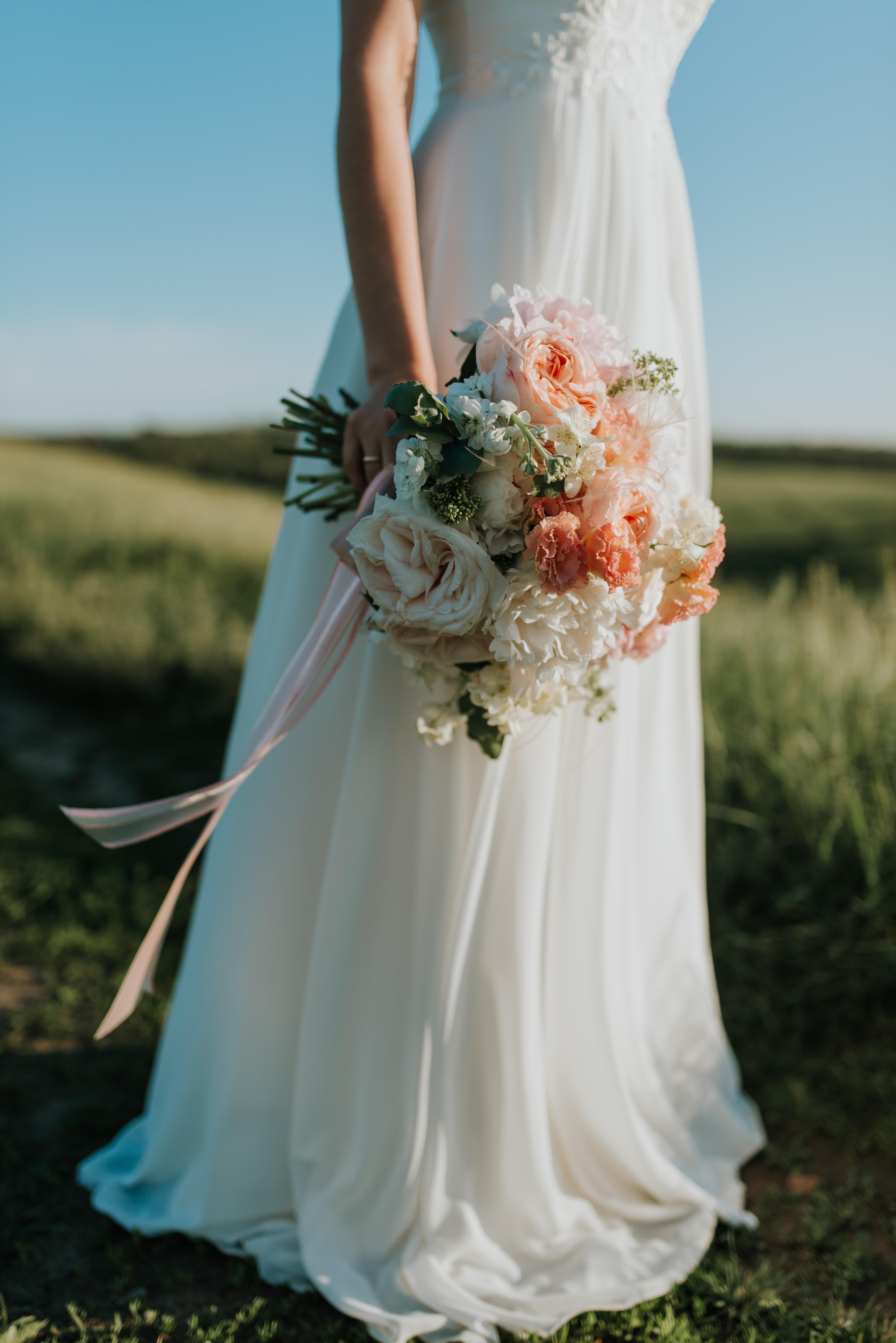 4735x7095 Woman Wearing White Wedding Dress Holding Flower Bouquet Standing on Green Field · Free