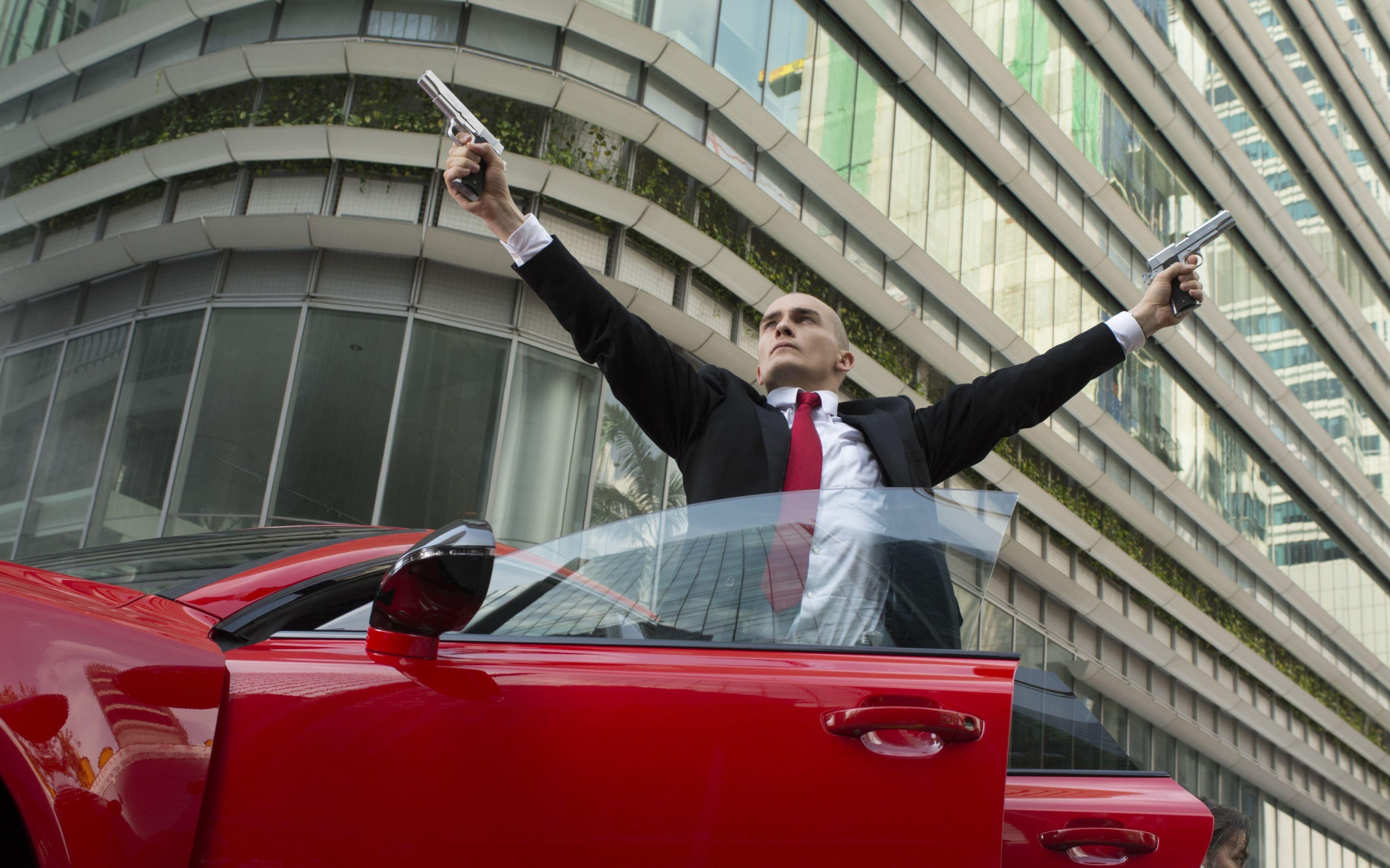 3840x2400 Hitman Agent 47 Rupert Friend Pointing Guns Pose Red Car Machine