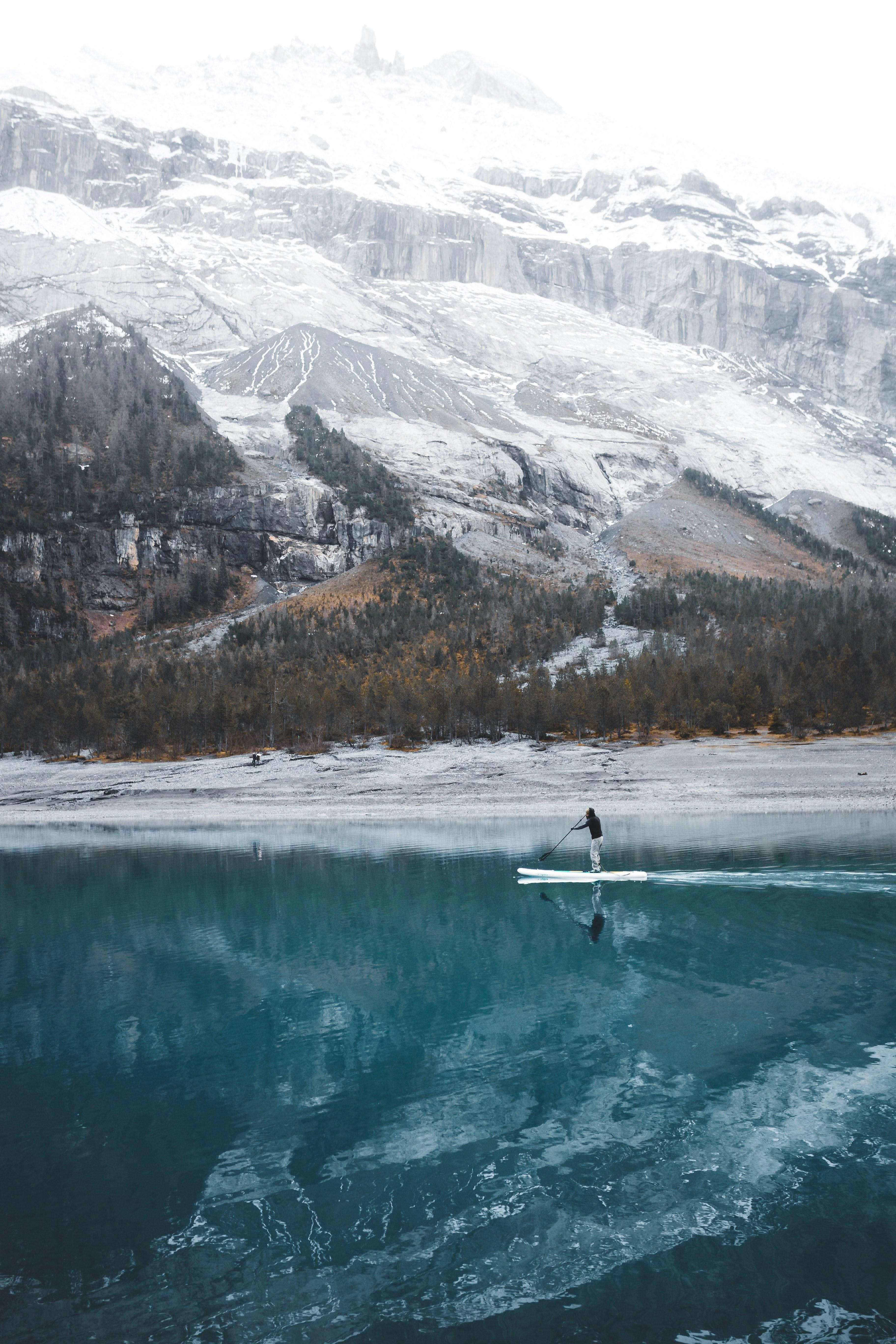 3648x5472 Wallpaper / a man on a paddle board on an azure lake in the mountains, paddling on the lake 4k wallpaper