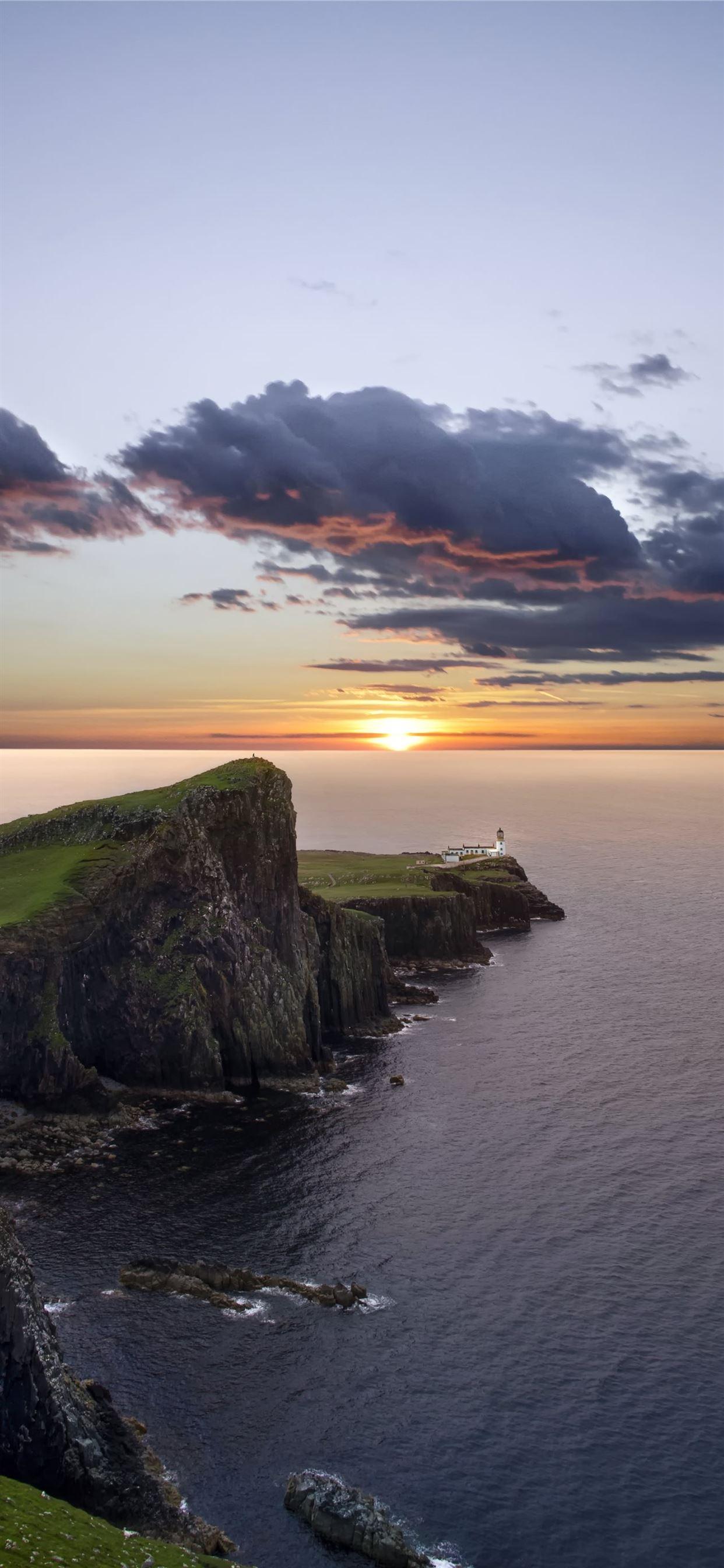 1242x2688 green and black mountain beside sea during sunset iPhone 11 Wallpaper Free Download